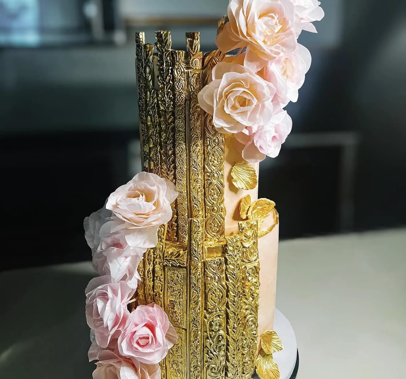 Side view of gold baroque tiered cake with blush roses cascading down ornate gilded panels