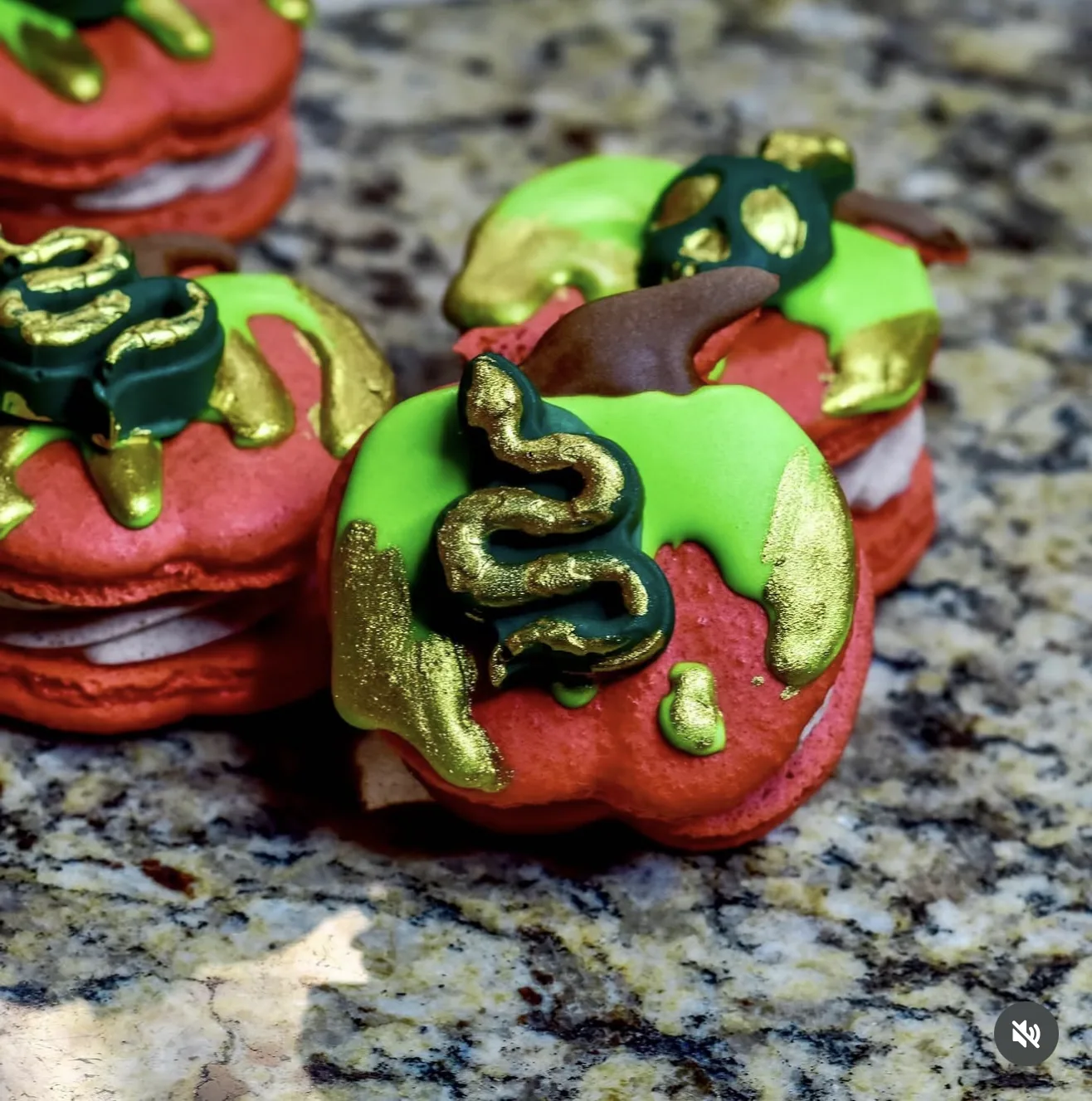 Red macarons topped with green poison drip and gold snake accents styled as poison apples