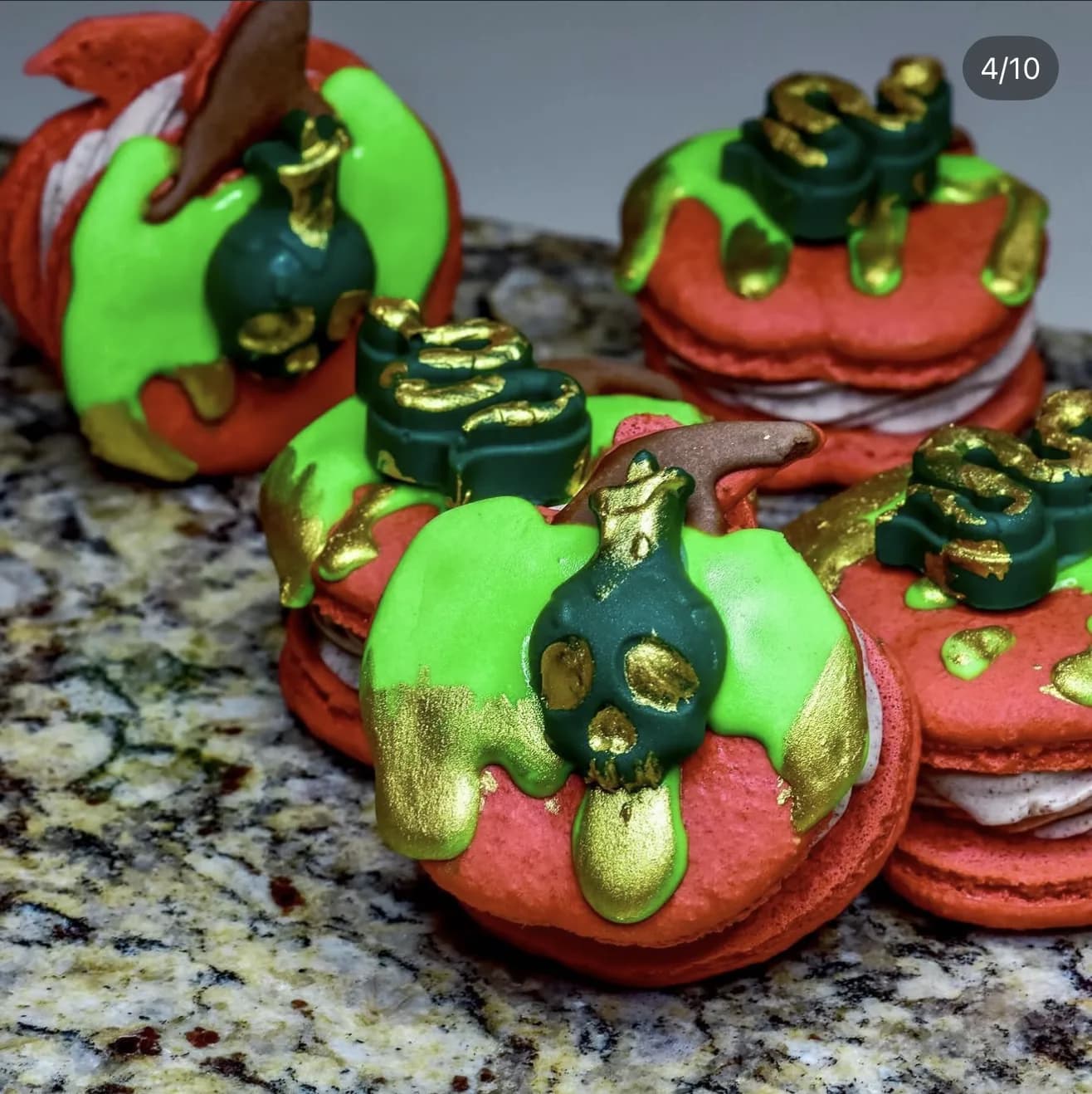 Grouped poison apple macarons with green drip and gold snakes on speckled granite surface