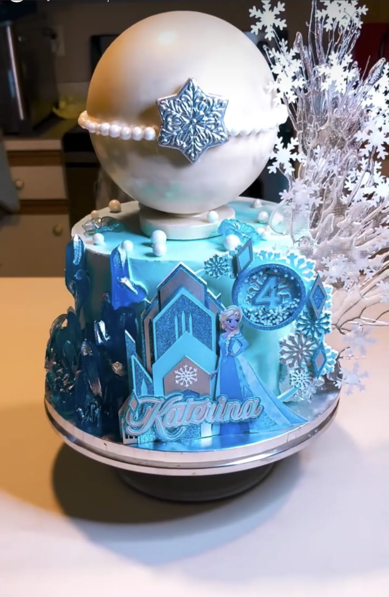 Two-tier Frozen-themed cake with ice castle, Elsa figure and large sphere topped with snowflake