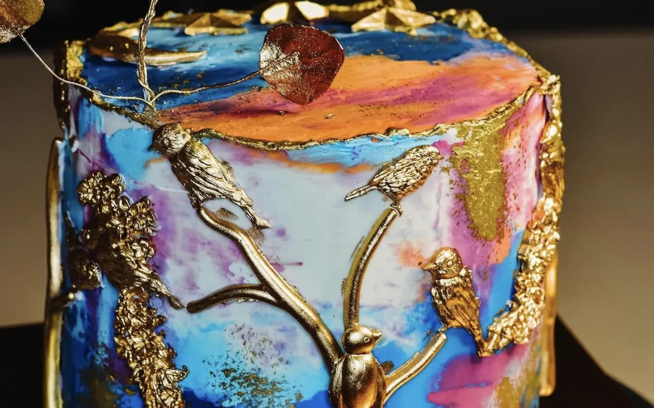Watercolor sunset cake with sculpted gold birds on branches and painterly blue pink clouds