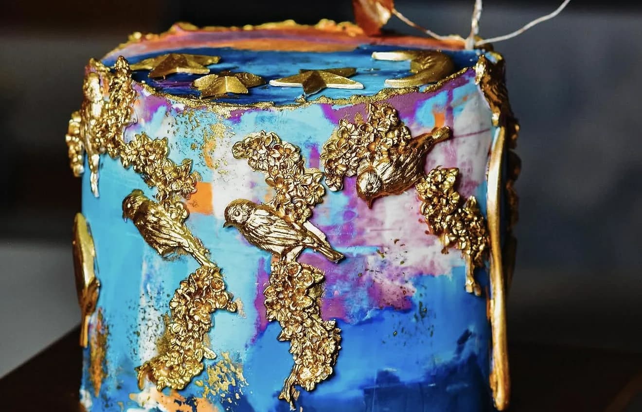 Close-up of gold sculpted birds on branches against painted blue and magenta cake background