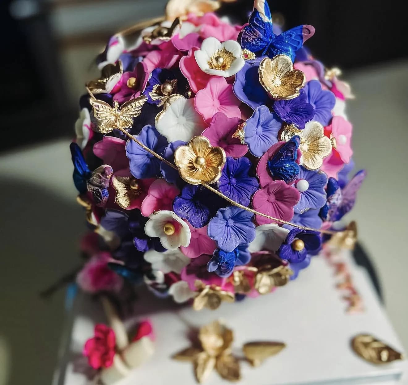 Sphere cake densely covered in pink purple sugar flowers with gold butterflies and leaves
