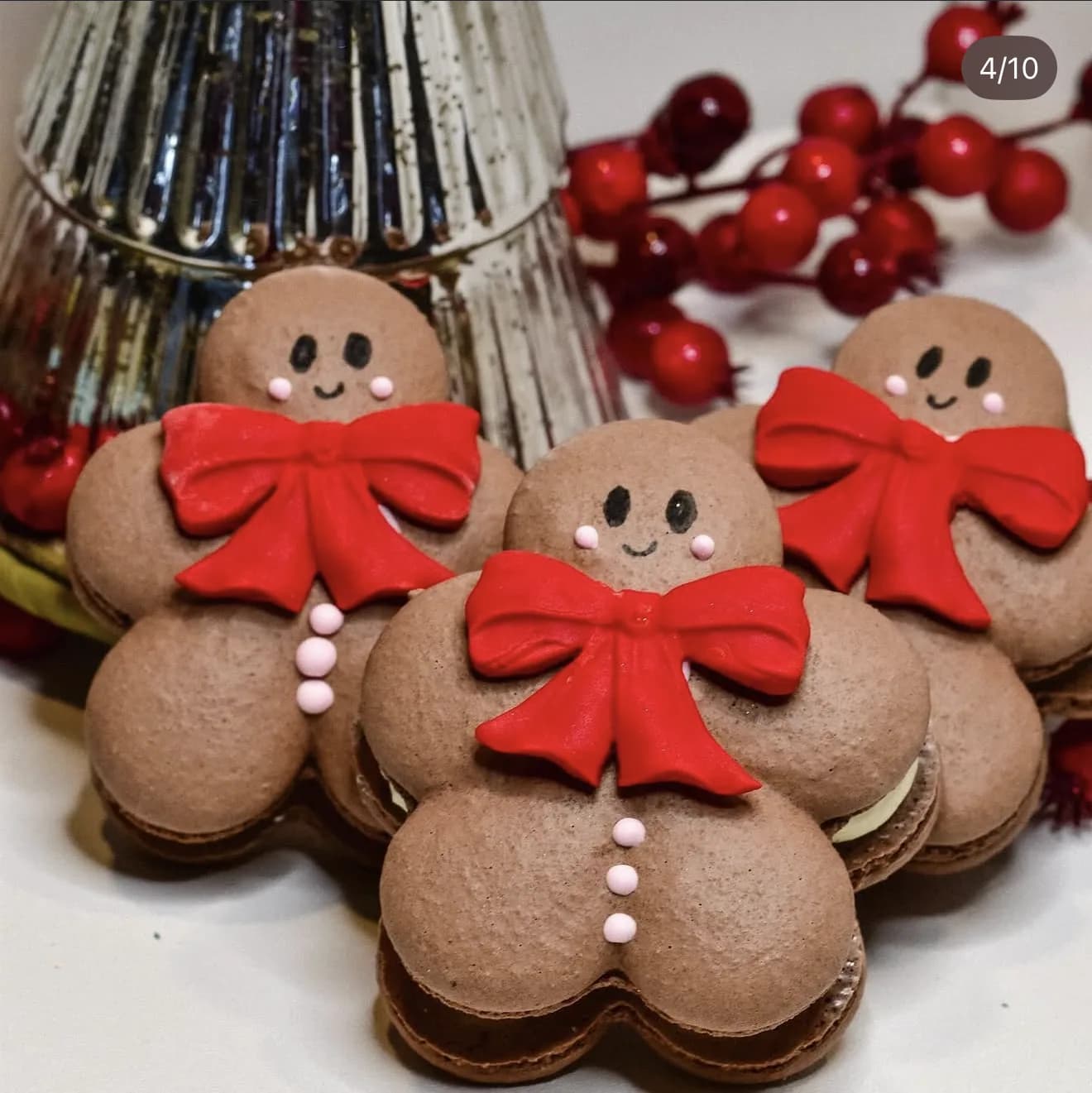 Three chocolate gingerbread-man shaped macarons with red fondant bows posed with red berries