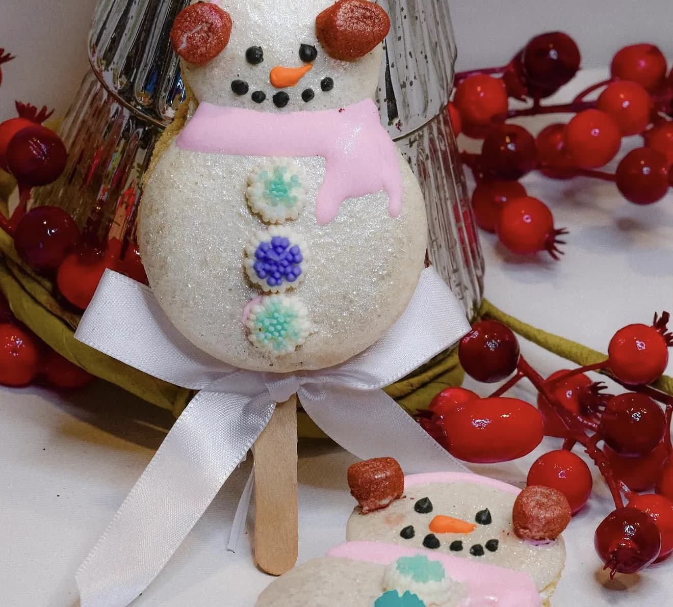 Glittered white snowman cakesicle with pink scarf and earmuffs tied with white bow and red berries