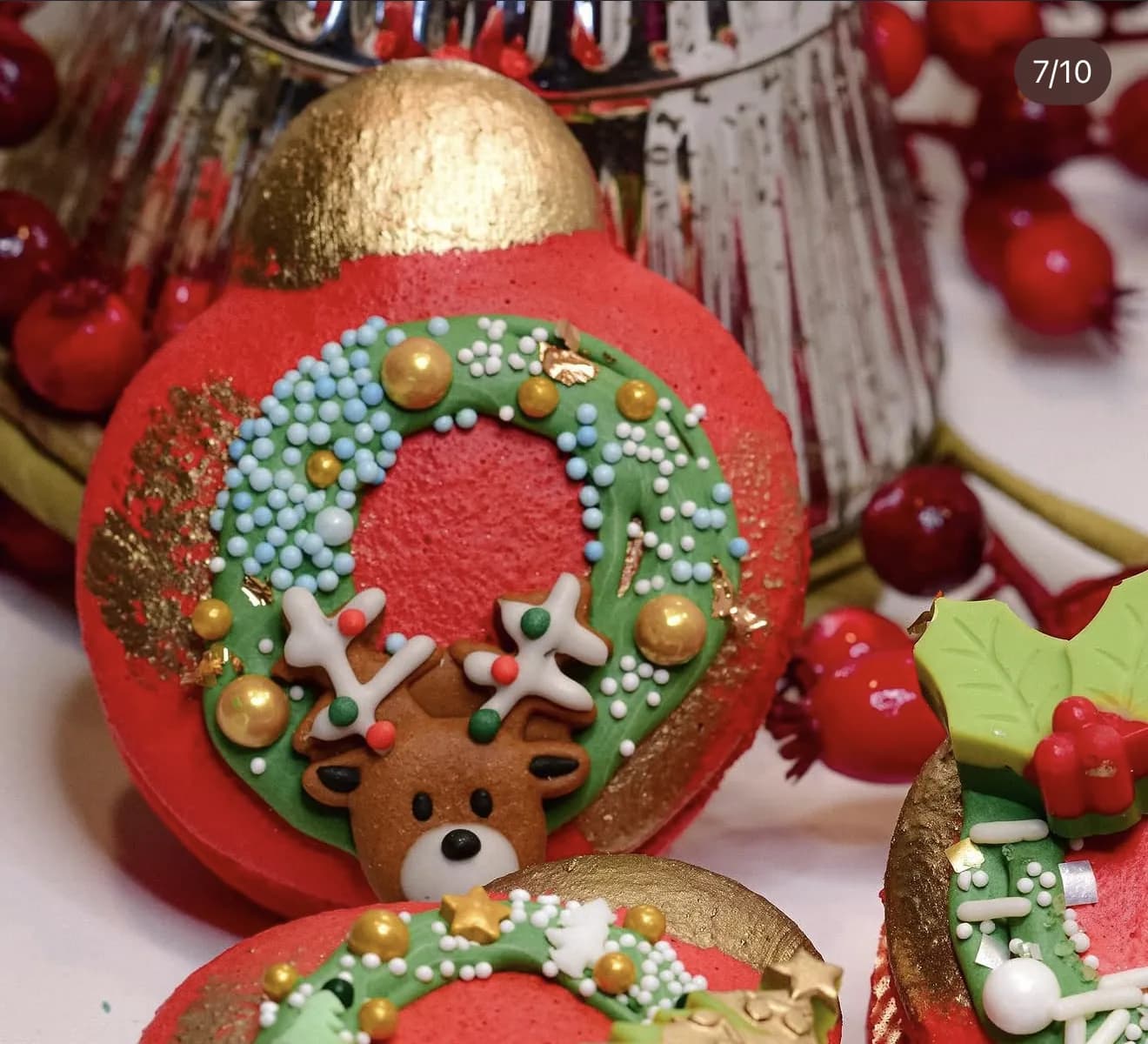 Red ornament-shaped macarons painted with green wreath and reindeer with gold leaf details