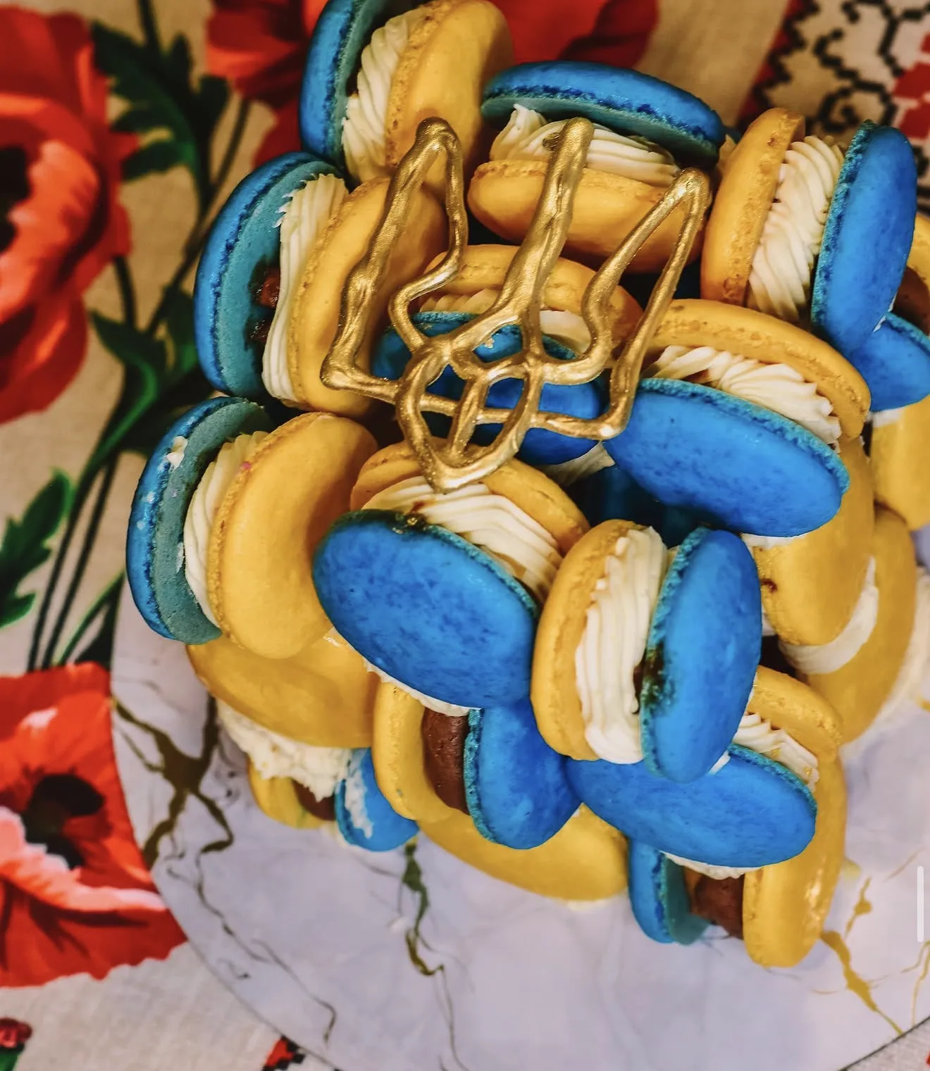 Stacked blue and yellow macaron tower with gold Ukrainian trident on poppy-print cloth