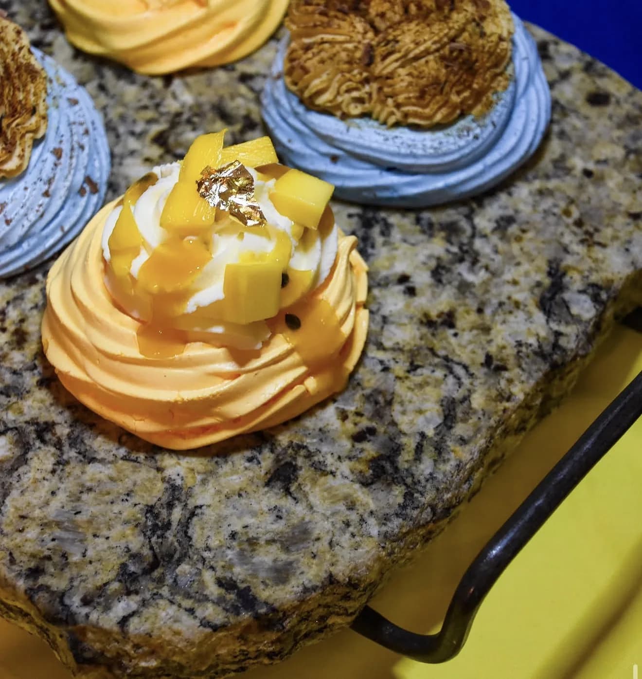 Individual pavlovas with orange meringue and fresh mango cubes gold leaf on granite