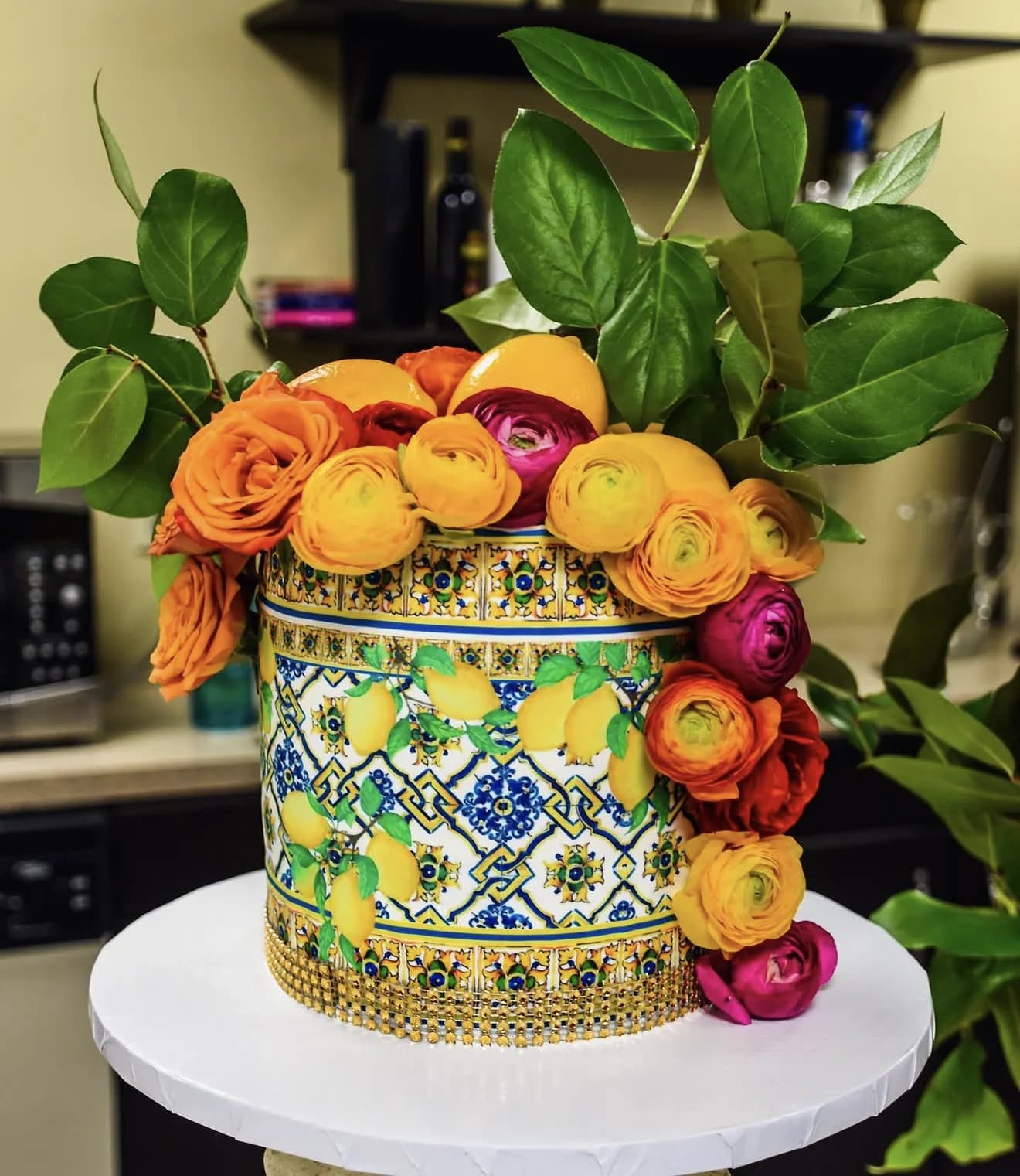 Tall cake hand-painted as blue yellow Sicilian majolica tile crowned with orange yellow ranunculus