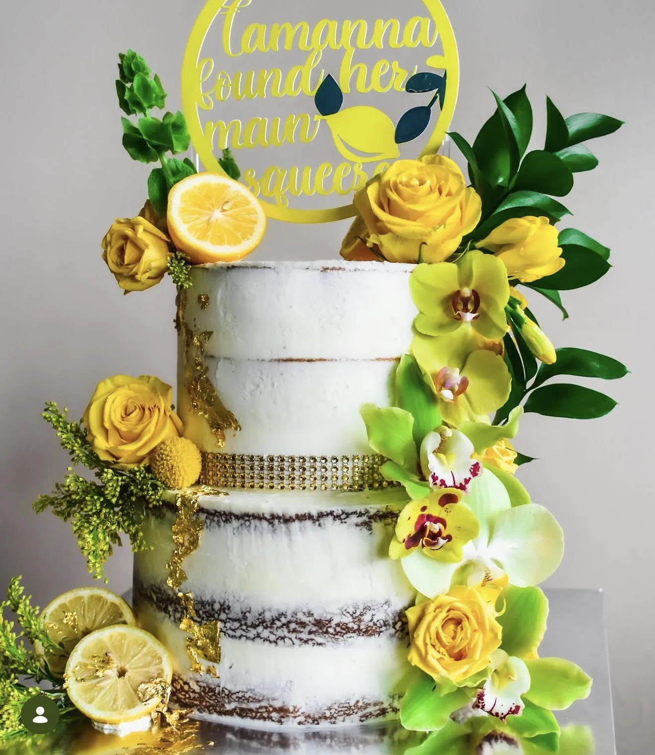Two-tier naked cake with gold belt accent topped with lemon slices yellow roses and orchids