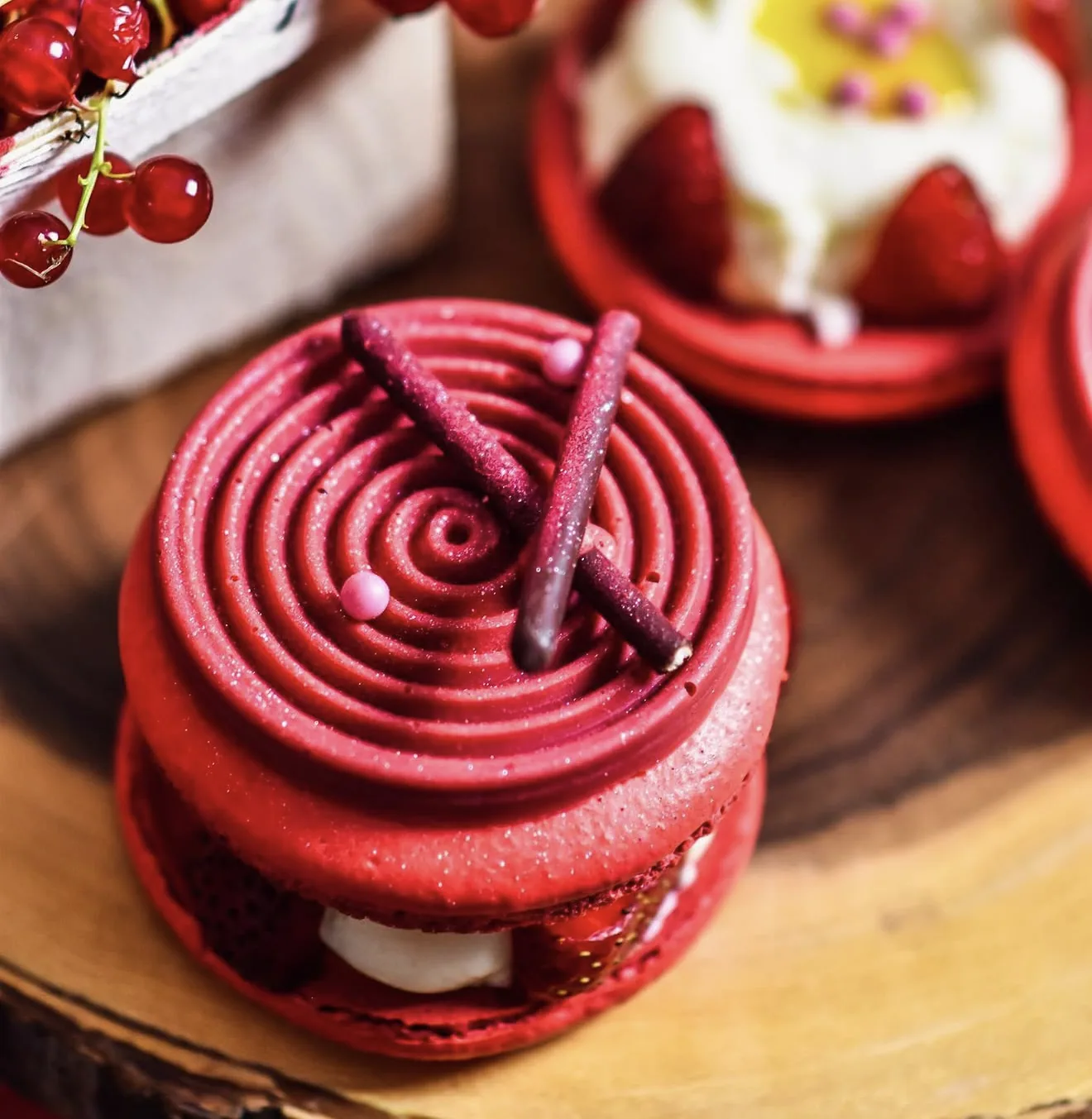 Macro shot of spiral piped red macaron with chocolate sticks and pink pearl detail