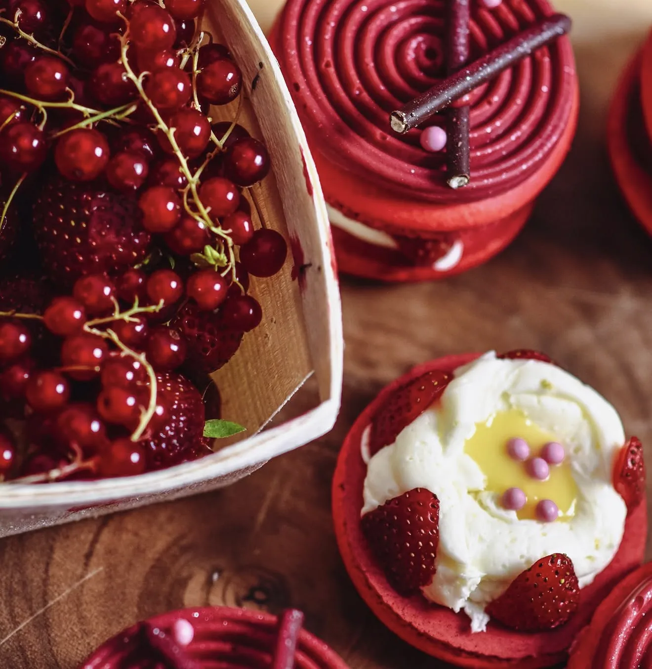 Overhead styled red macarons and open-face cream tart with strawberries and currants