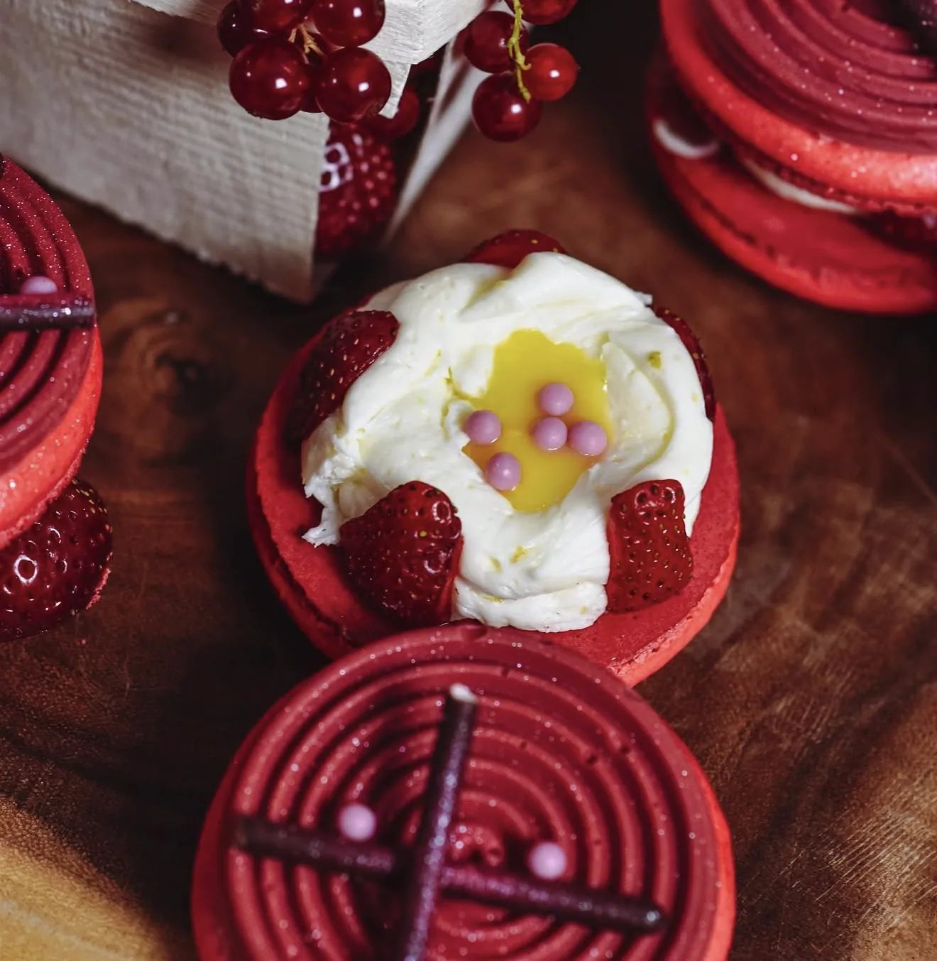 Open red macaron base filled with cream lemon curd pearls surrounded by currants