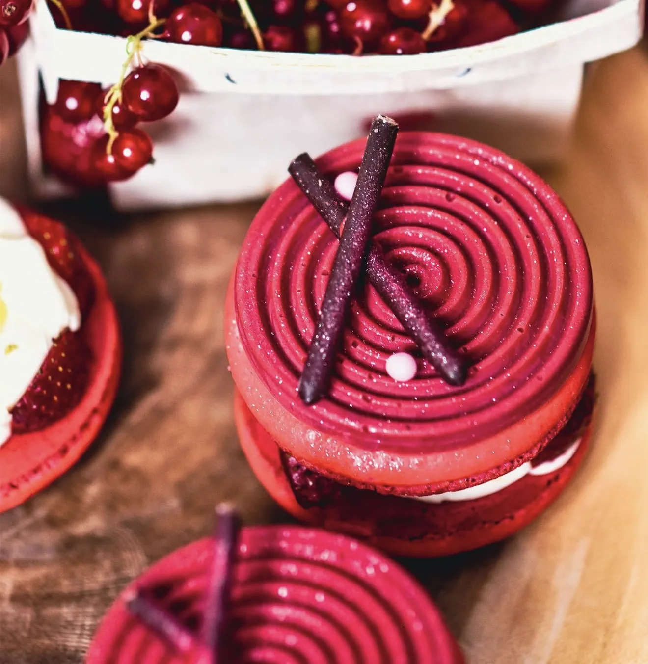 Close-up of magenta spiral piped macaron with chocolate sticks against rustic wood board