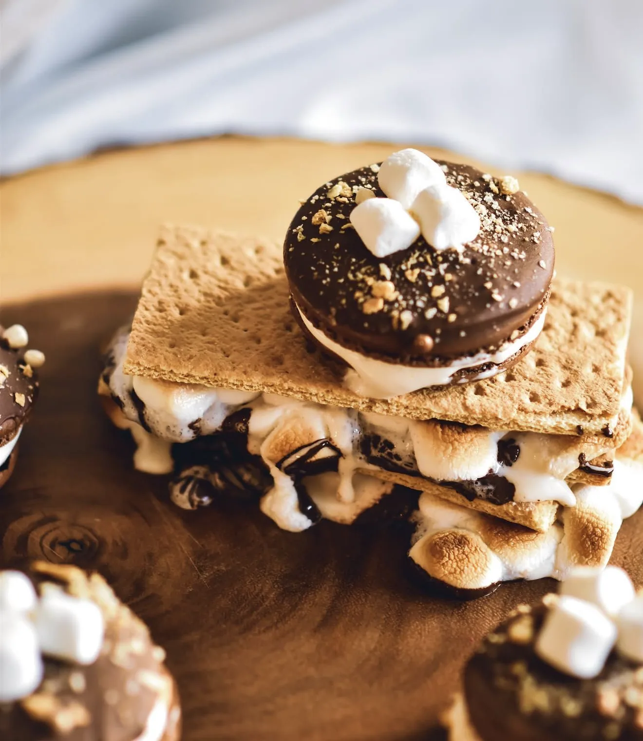 Chocolate smores macaron topped with mini marshmallows layered on toasted marshmallow graham cracker