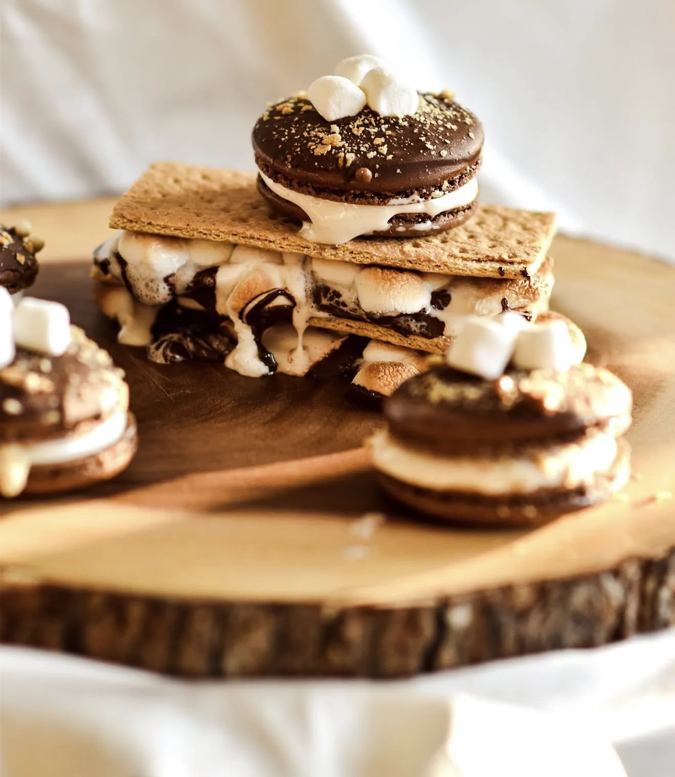 Smores macaron tower stacked on toasted marshmallow and graham crackers on rustic wood slab