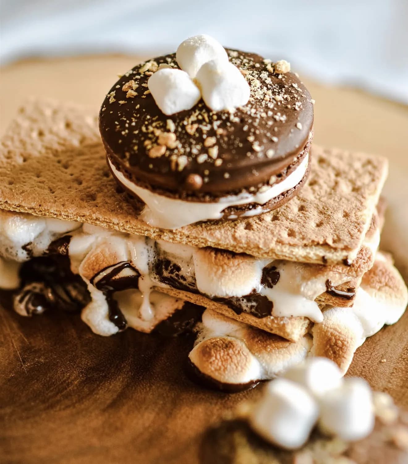 Smores macaron hero with melty marshmallows escaping graham cracker and chocolate drizzle