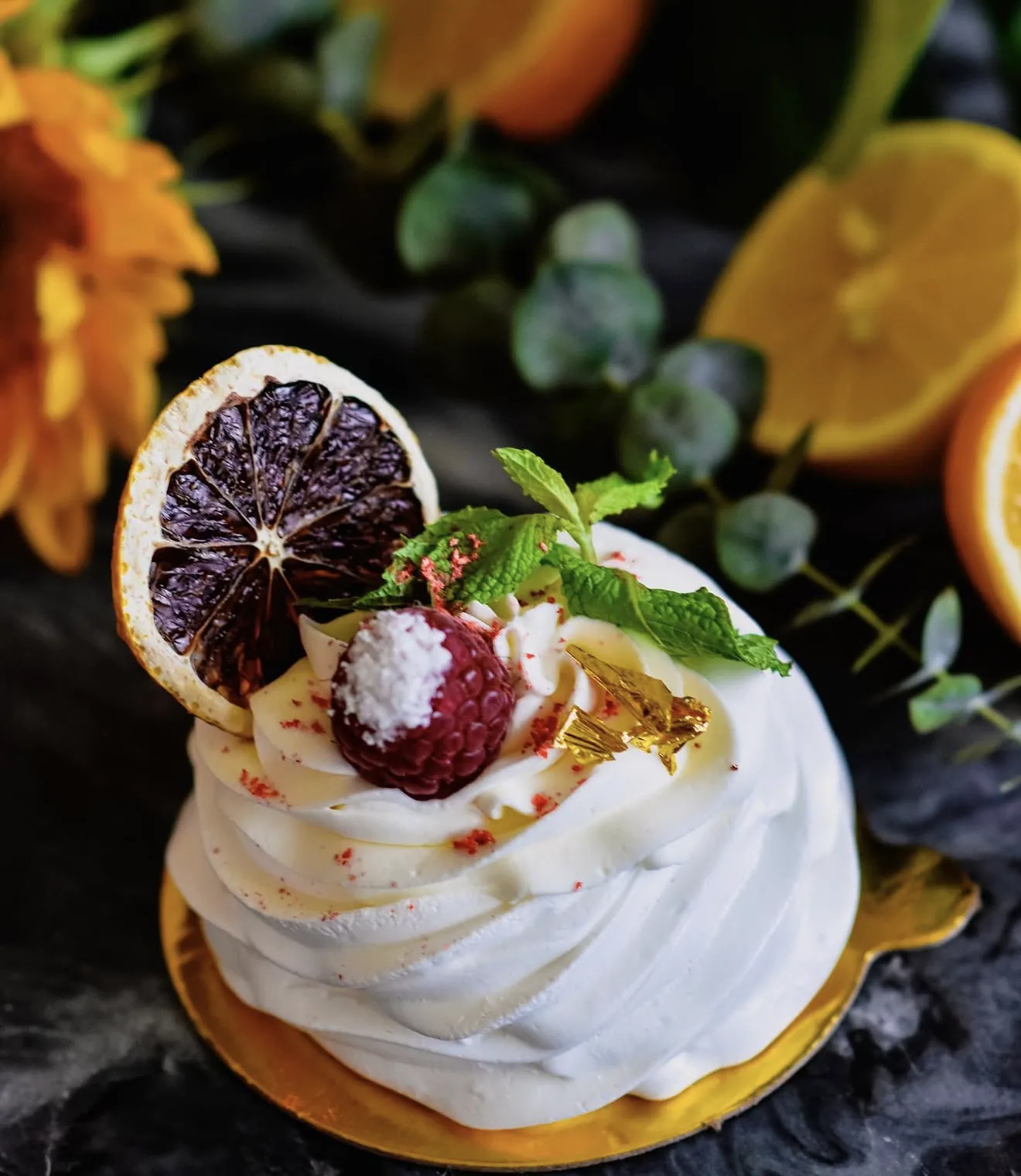 Mini pavlova with blood orange slice raspberry coconut ball mint and gold leaf on marble