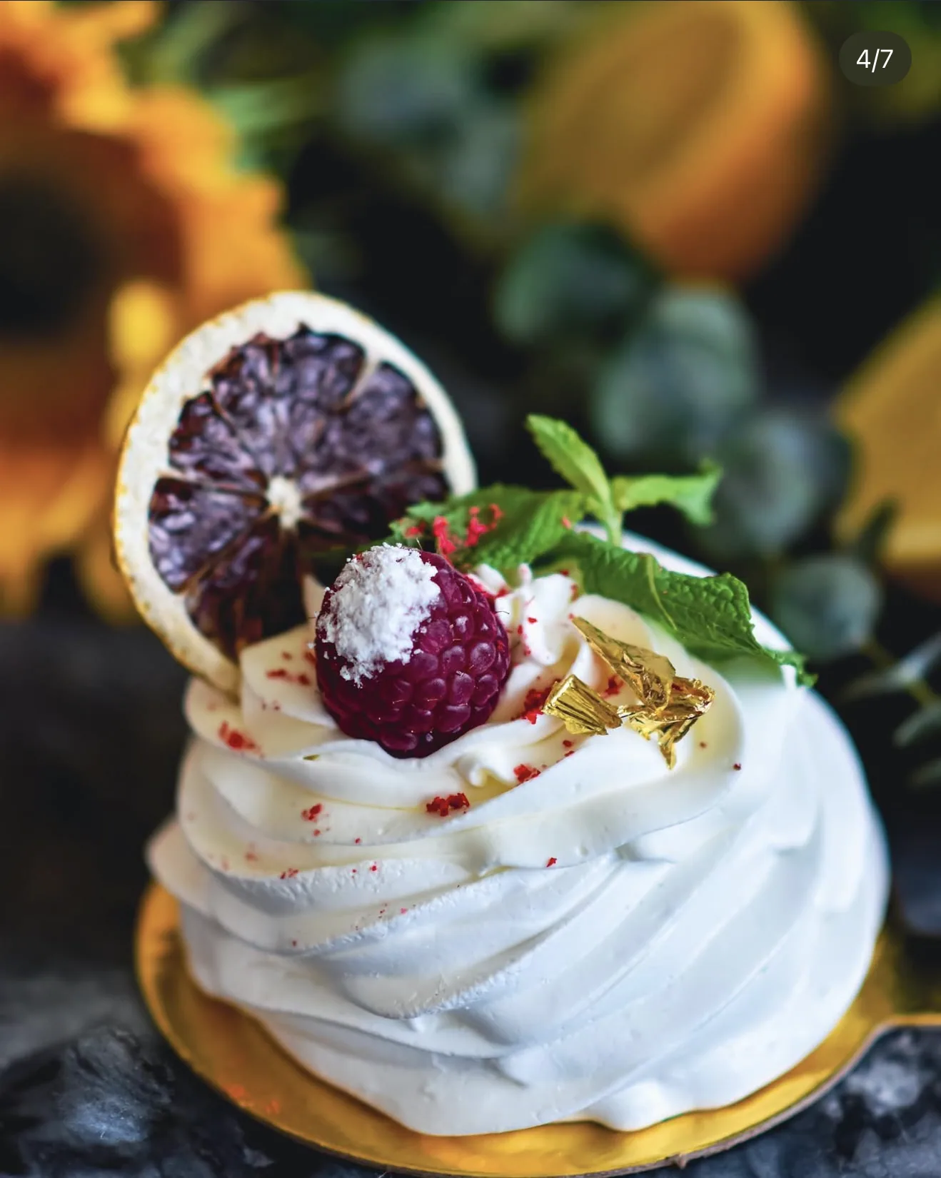 Side view pavlova with blood orange chip and coconut coated raspberry and gold foil