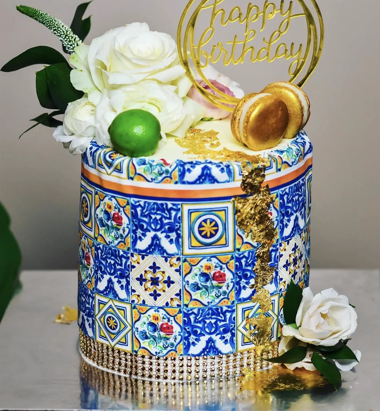 Blue Moroccan tile painted cake with gold leaf drip white roses and lime macaron topper