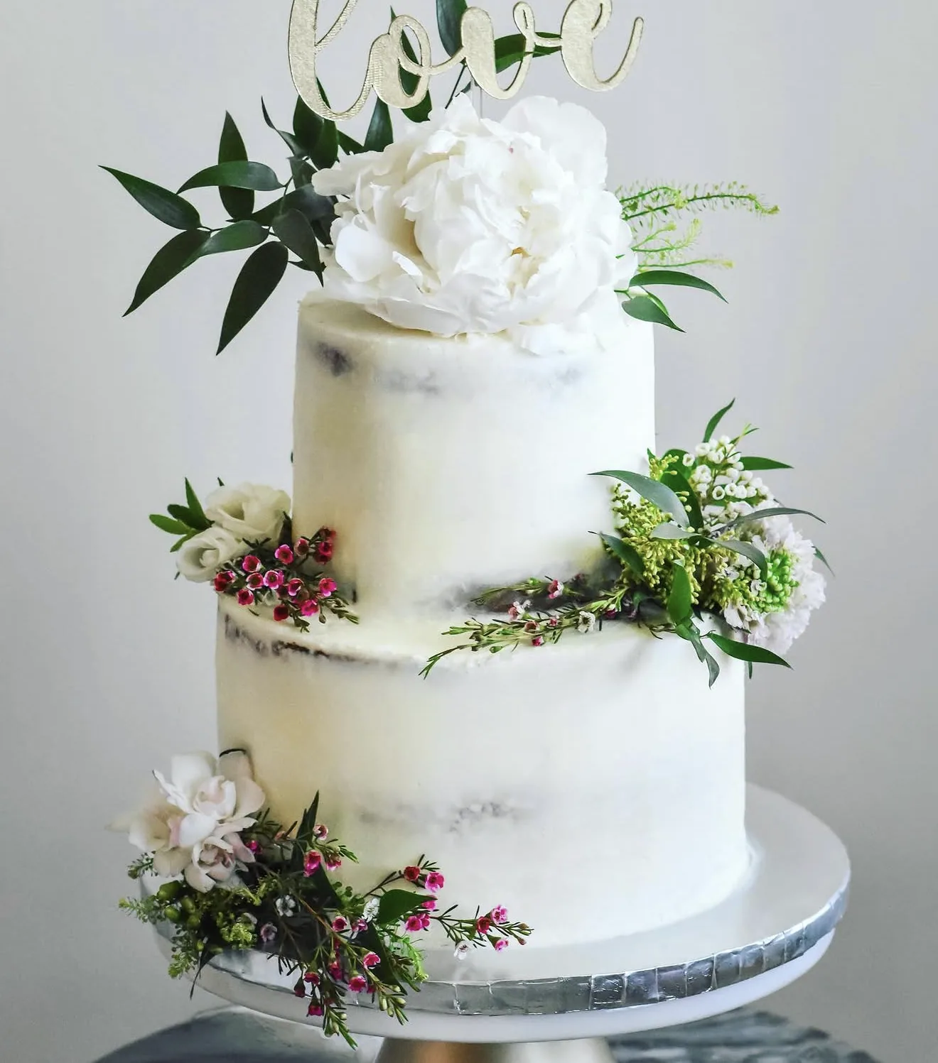 Two-tier semi-naked cake with gold love topper peonies waxflowers and greenery