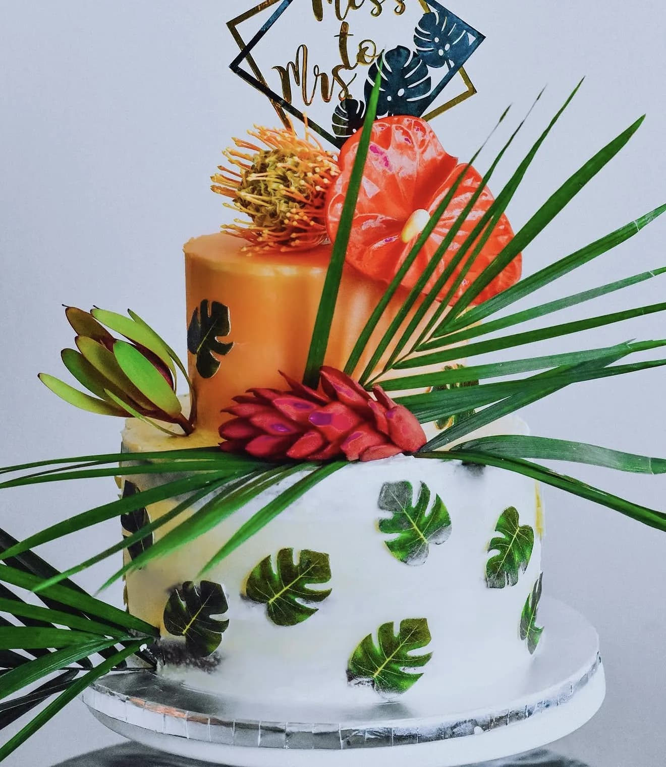 Two-tier cake with coral anthurium monstera leaf impressions and Miss to Mrs geometric topper