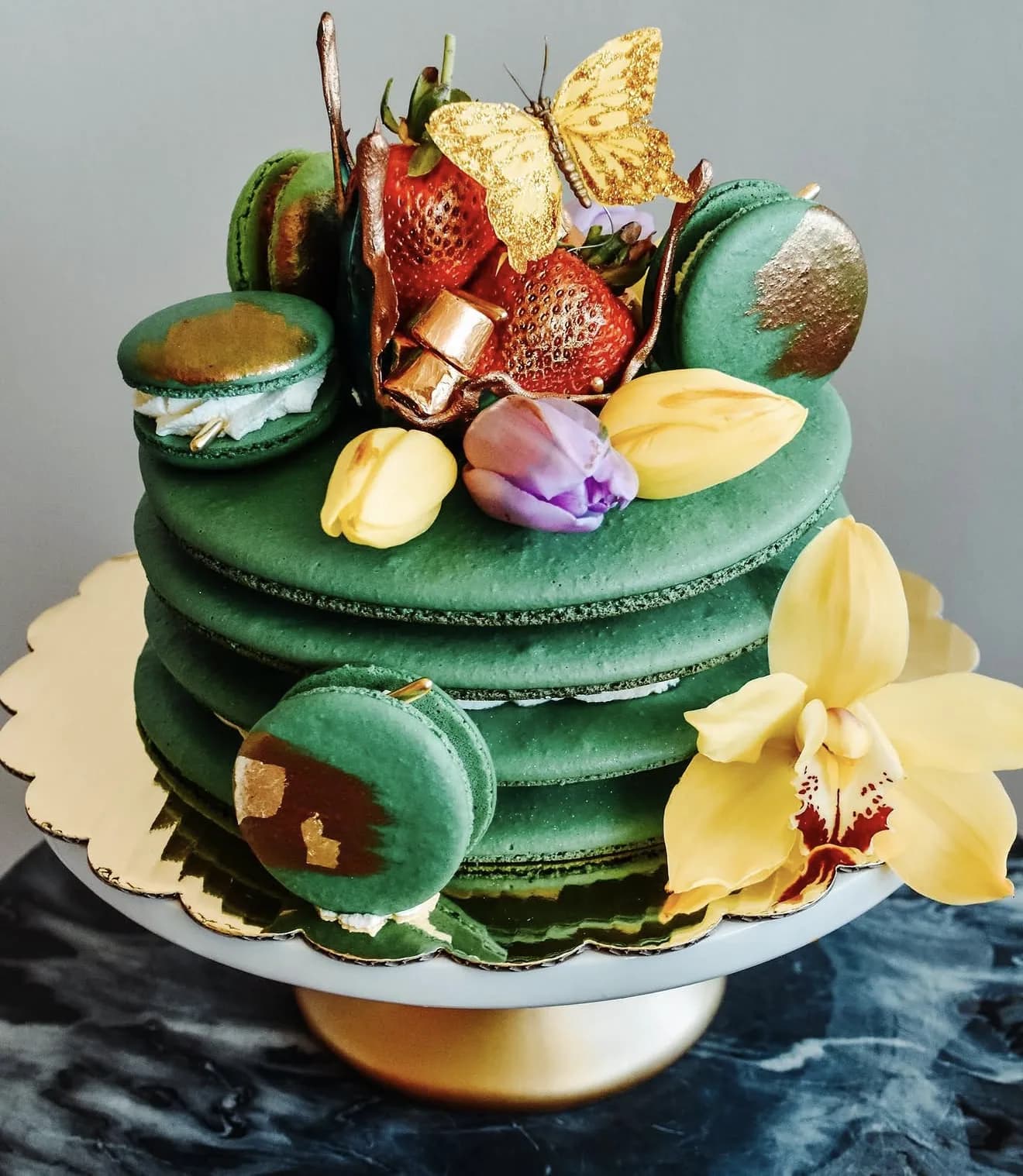 Front view emerald macaron cake with gold leaf strawberry butterfly and tulip tropical accents
