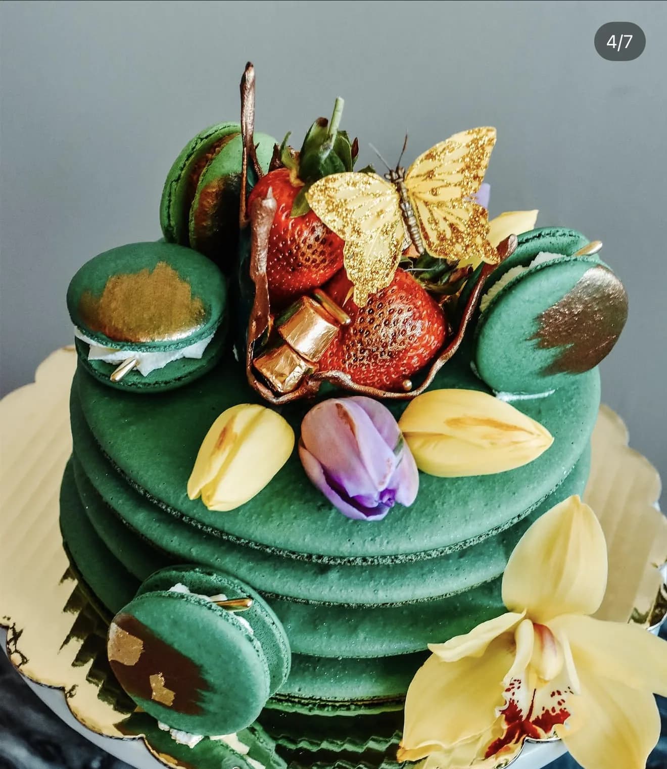 Wide shot of emerald macaron cake on stand with strawberries gold butterfly and orchid
