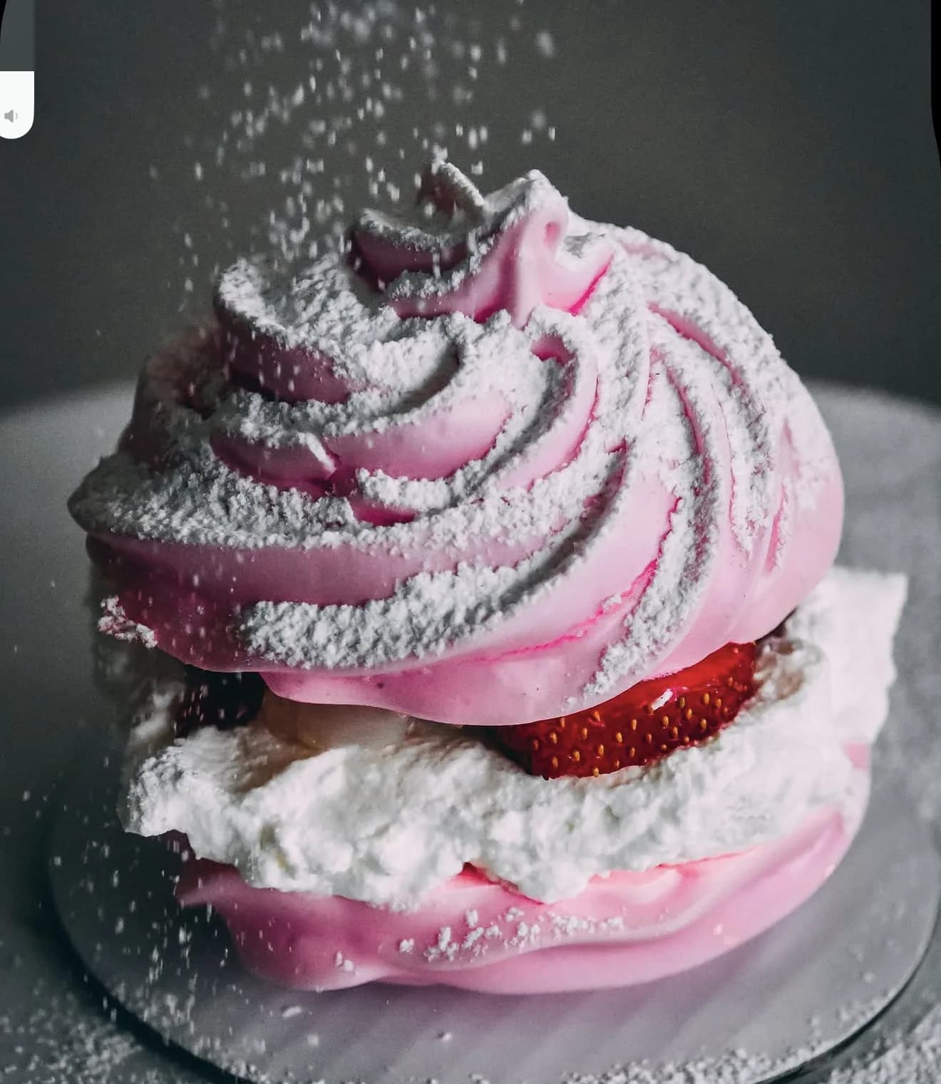 Pink pavlova with cascading powdered sugar peaked meringue and strawberry cream filling