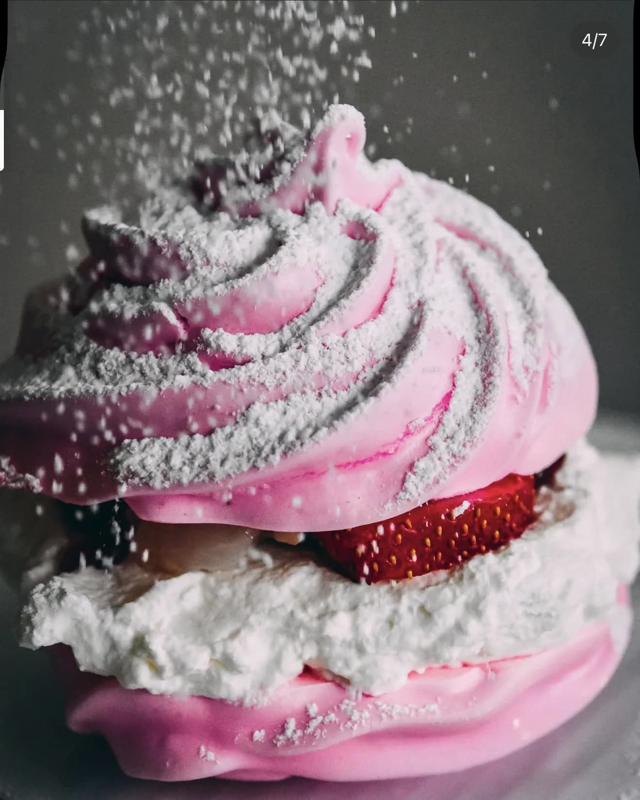 Close angle pink pavlova with cascading sugar strawberry slice and cream overflowing