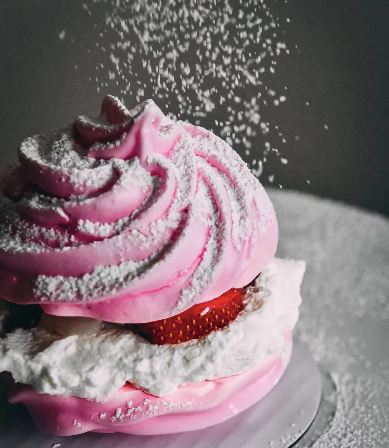 Macro pink pavlova with pillowy peaked meringue cascading sugar and strawberry fruit filling
