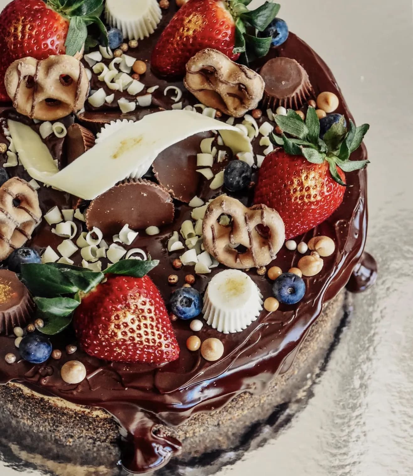 Overhead chocolate ganache cake with pretzel toppings strawberries blueberries and curls