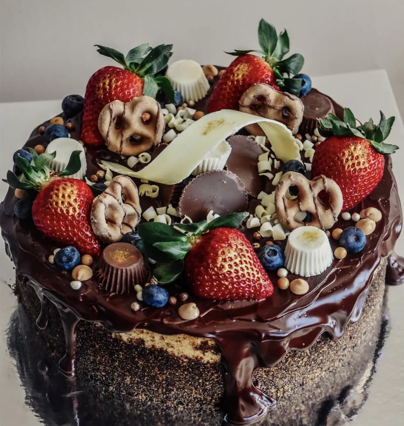 Overhead chocolate ganache cake garnished with pretzels chocolate cups strawberries blueberries