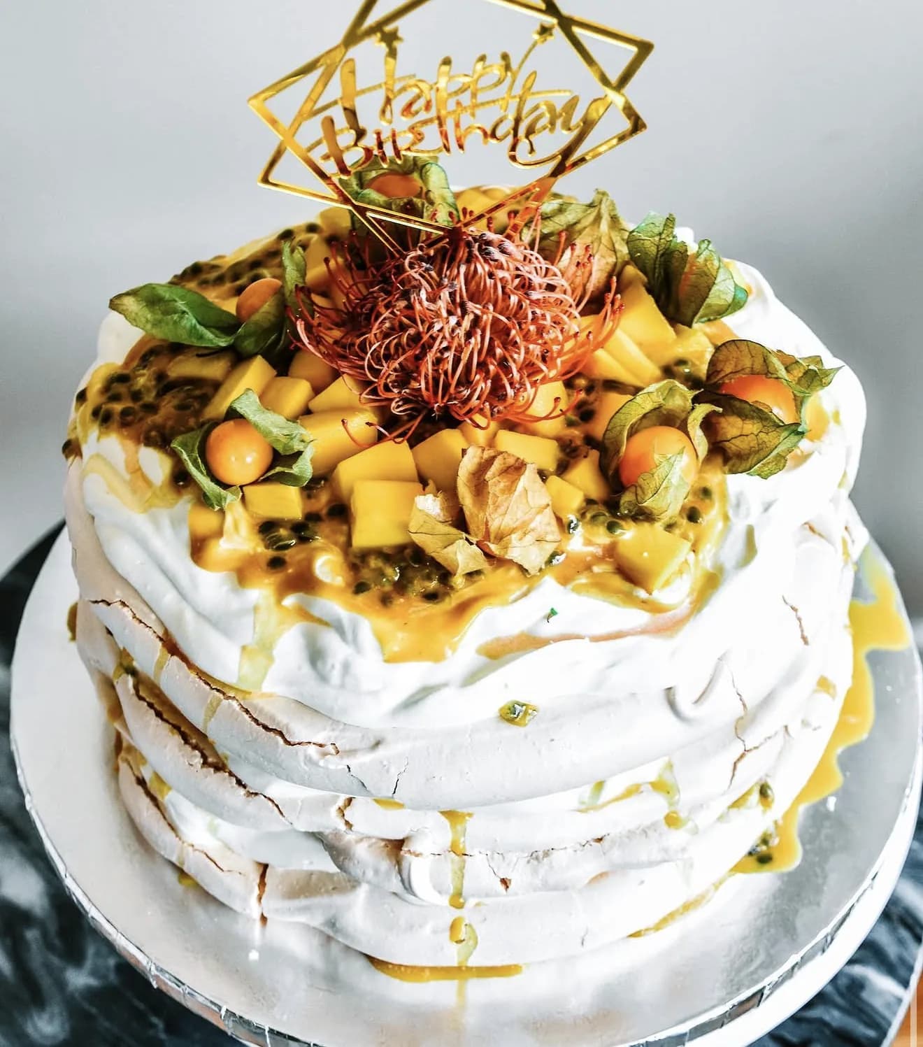 Stacked pavlova tower with mango cubes passionfruit protea and Happy Birthday geometric topper