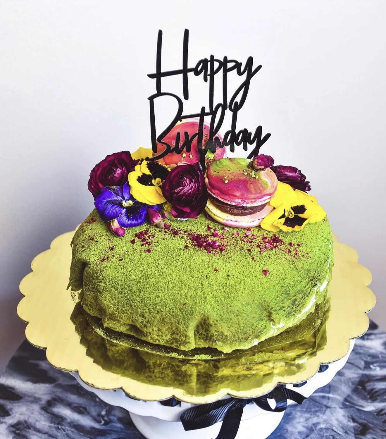 Matcha naked cake dusted green topped with pansies marbled macaron and Happy Birthday topper