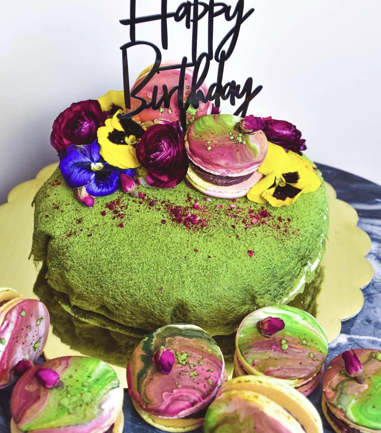 Matcha dusted naked cake with pansies marbled pink green macarons and red edible petals