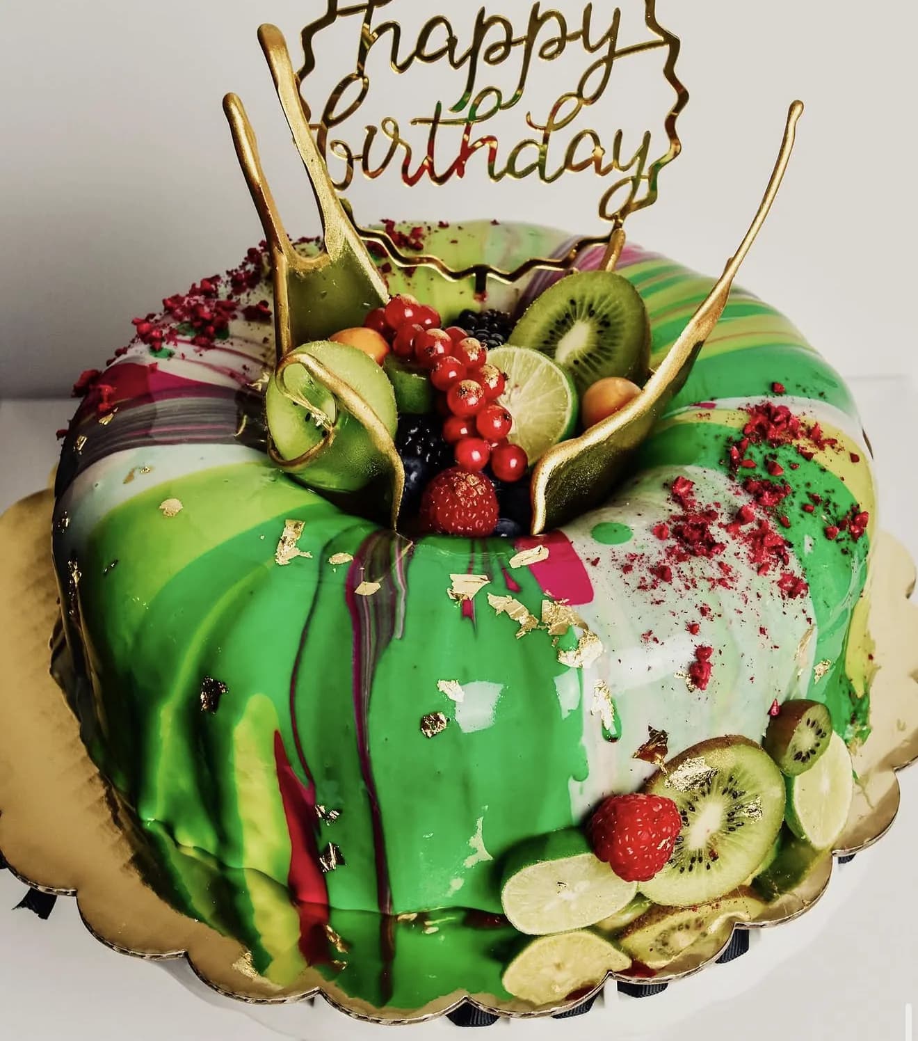 Green marble mirror glaze cake topped with kiwi lime berries gold leaf and Happy Birthday hoop