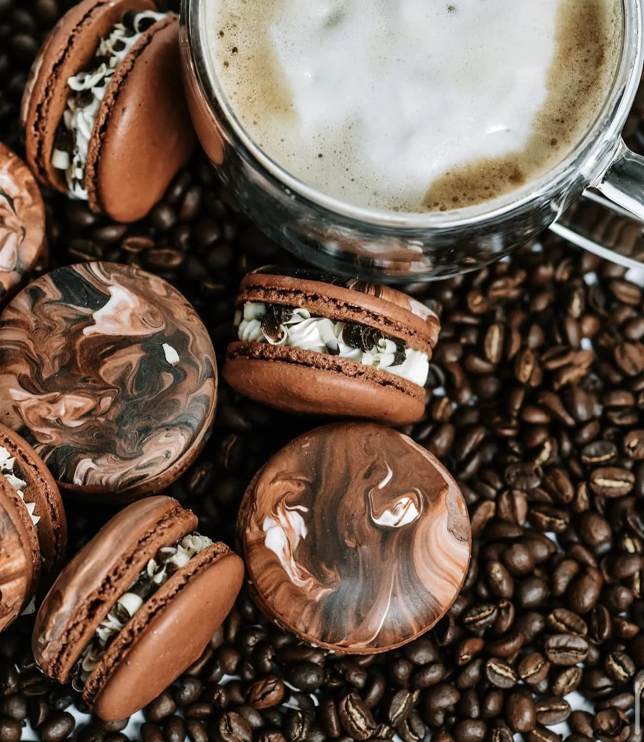 Marbled chocolate macarons with espresso bean drizzle and fresh coffee latte mug backdrop