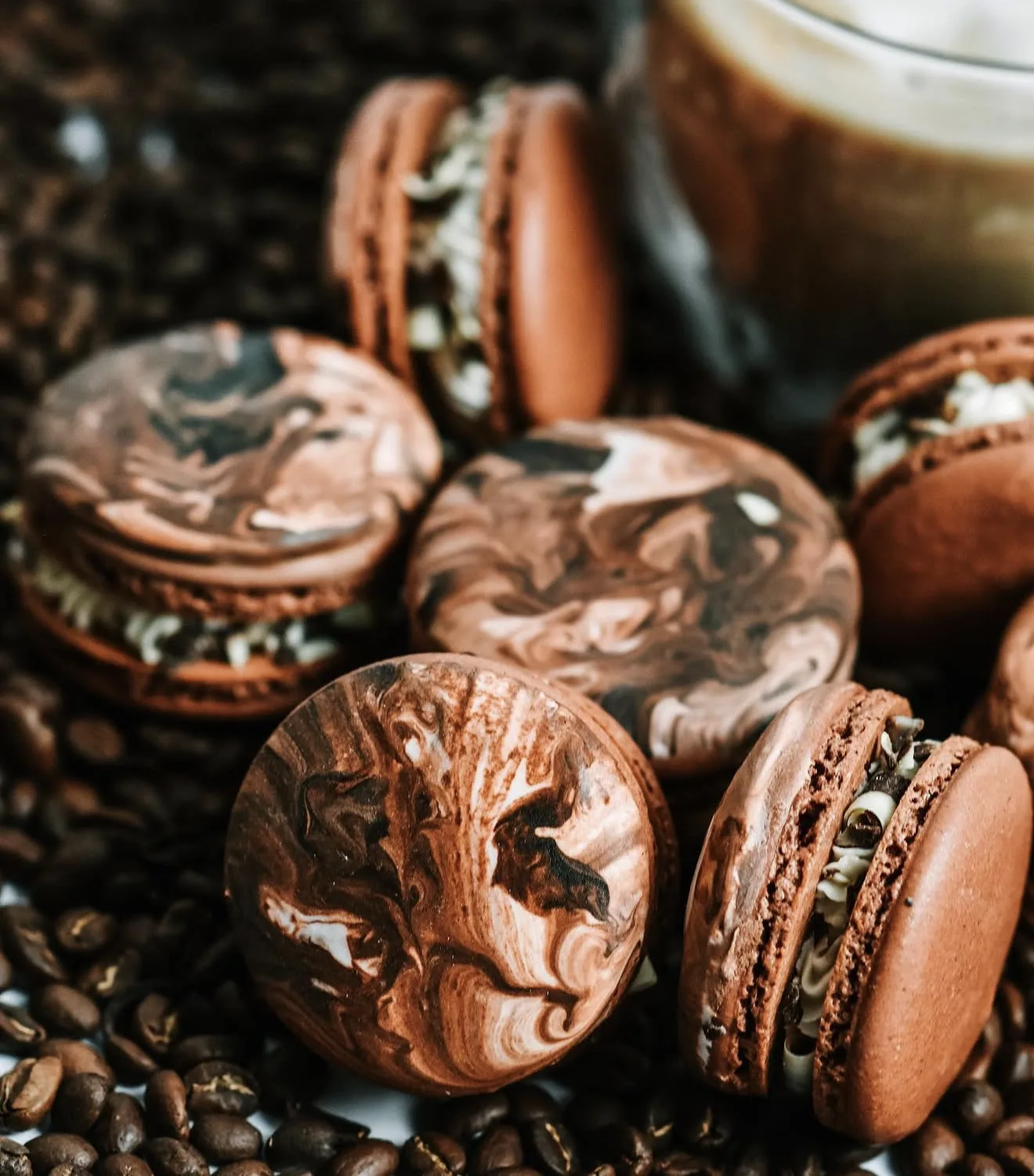 Pile of marbled mocha macarons resting on scattered coffee beans with espresso glass