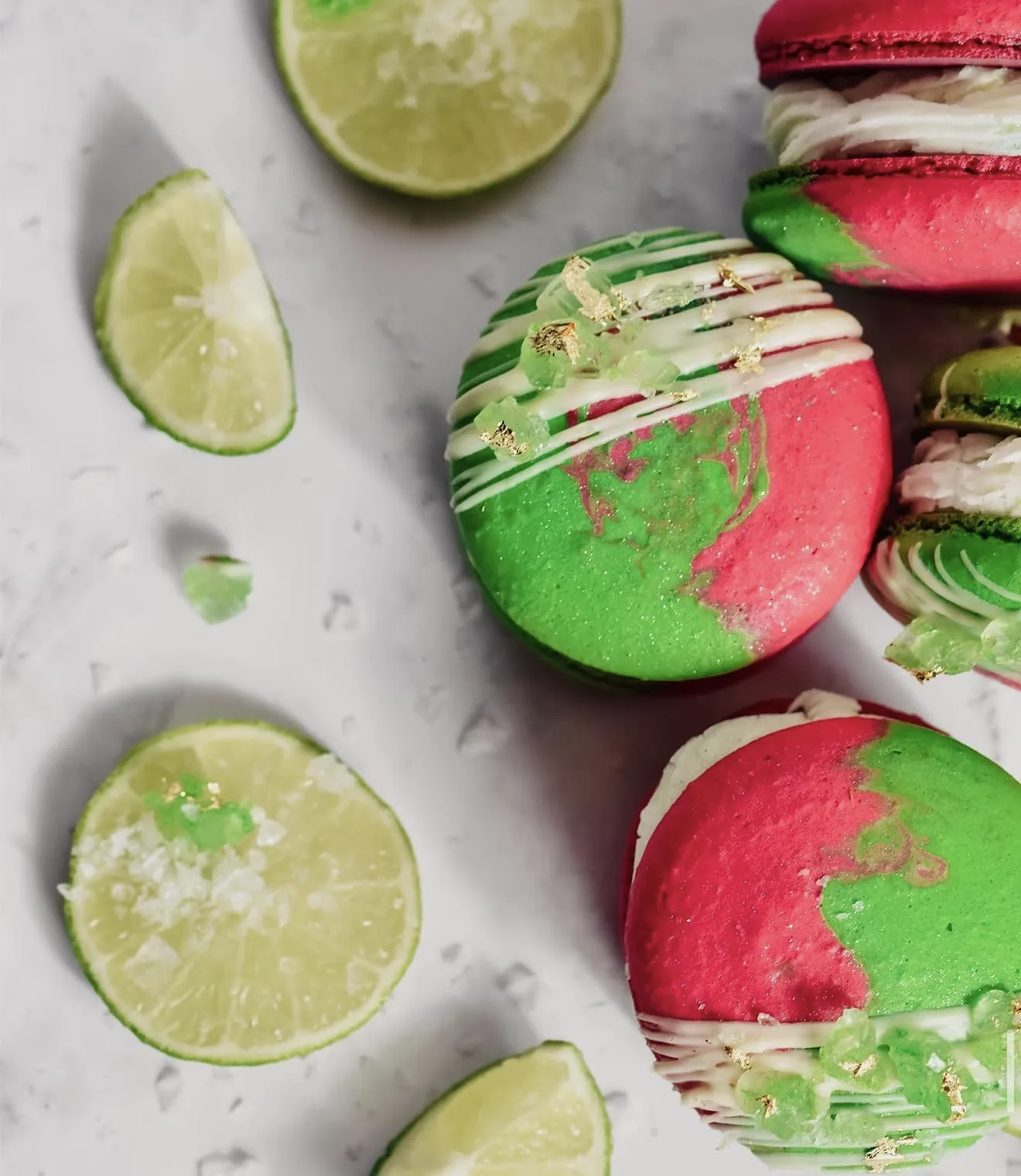 Overhead pink and green lime macarons with sliced limes scattered on speckled surface