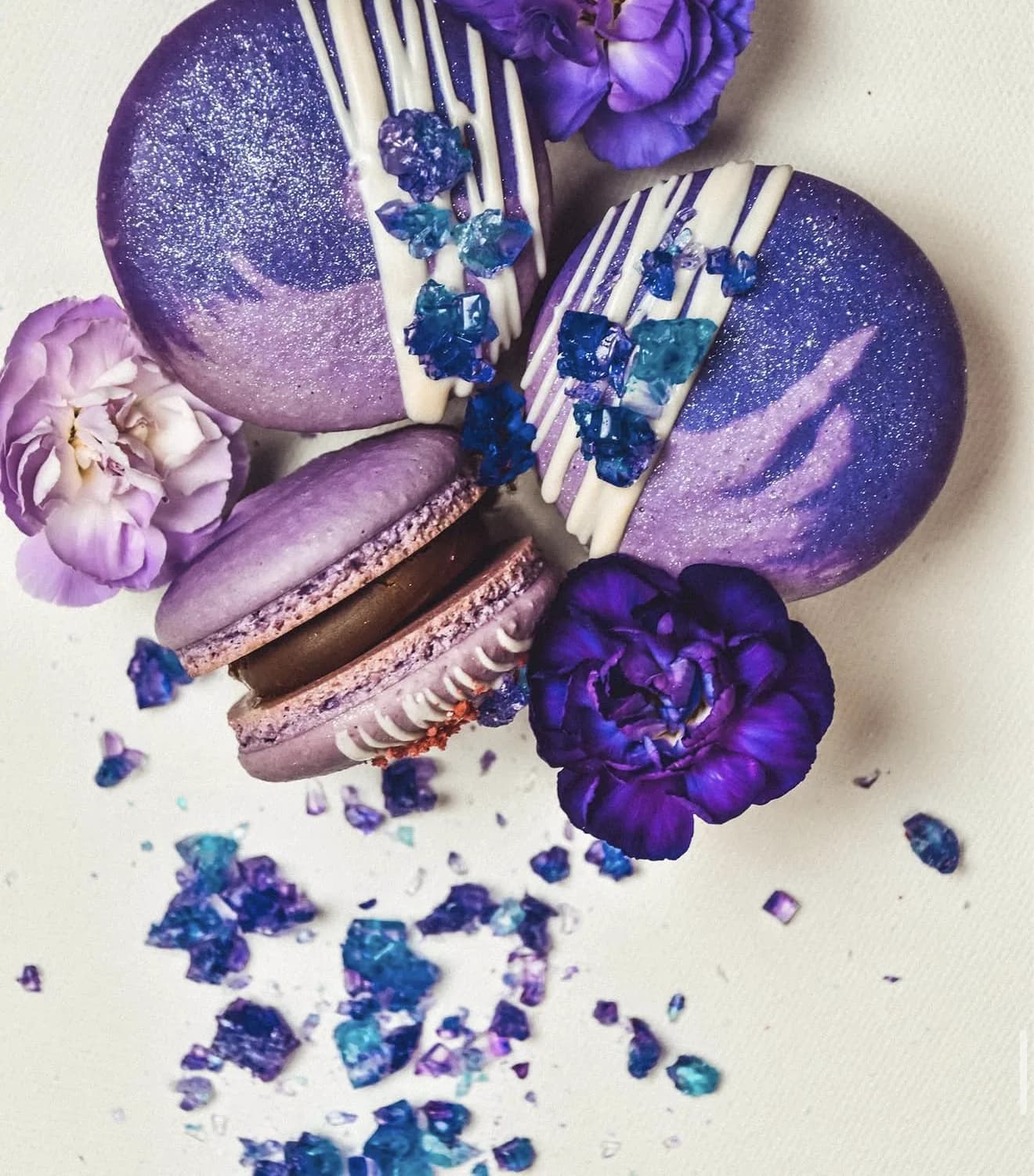 Purple shimmer macarons with white chocolate drip and blue amethyst sugar crystals plus violet florals