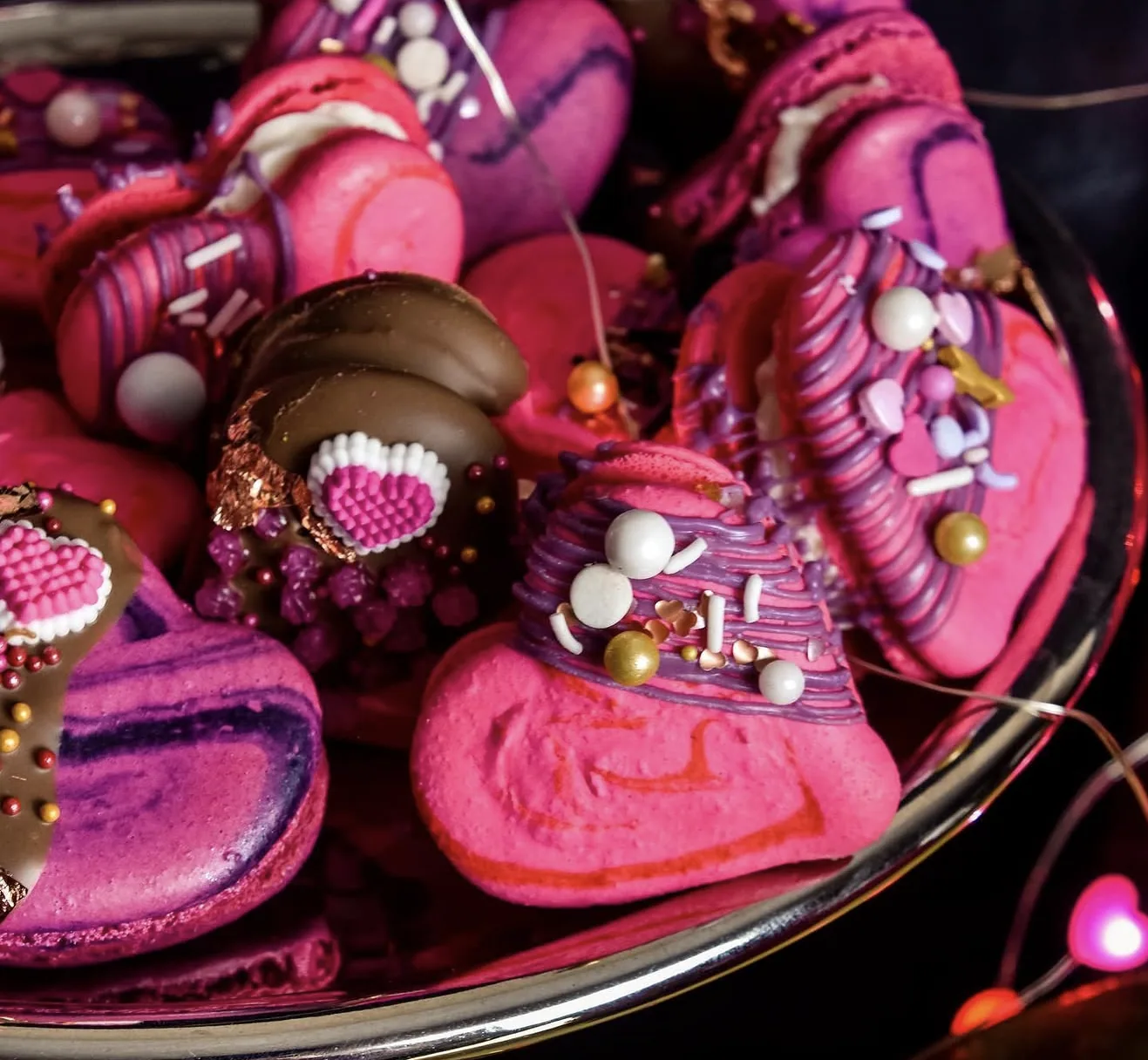 Pink and purple macarons shaped as witch hats with sprinkles and piped hearts on silver tray