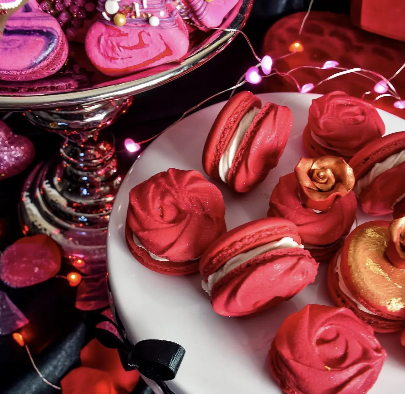 Front view red piped rose macarons beside pink roses and gold leaf accented red macaron