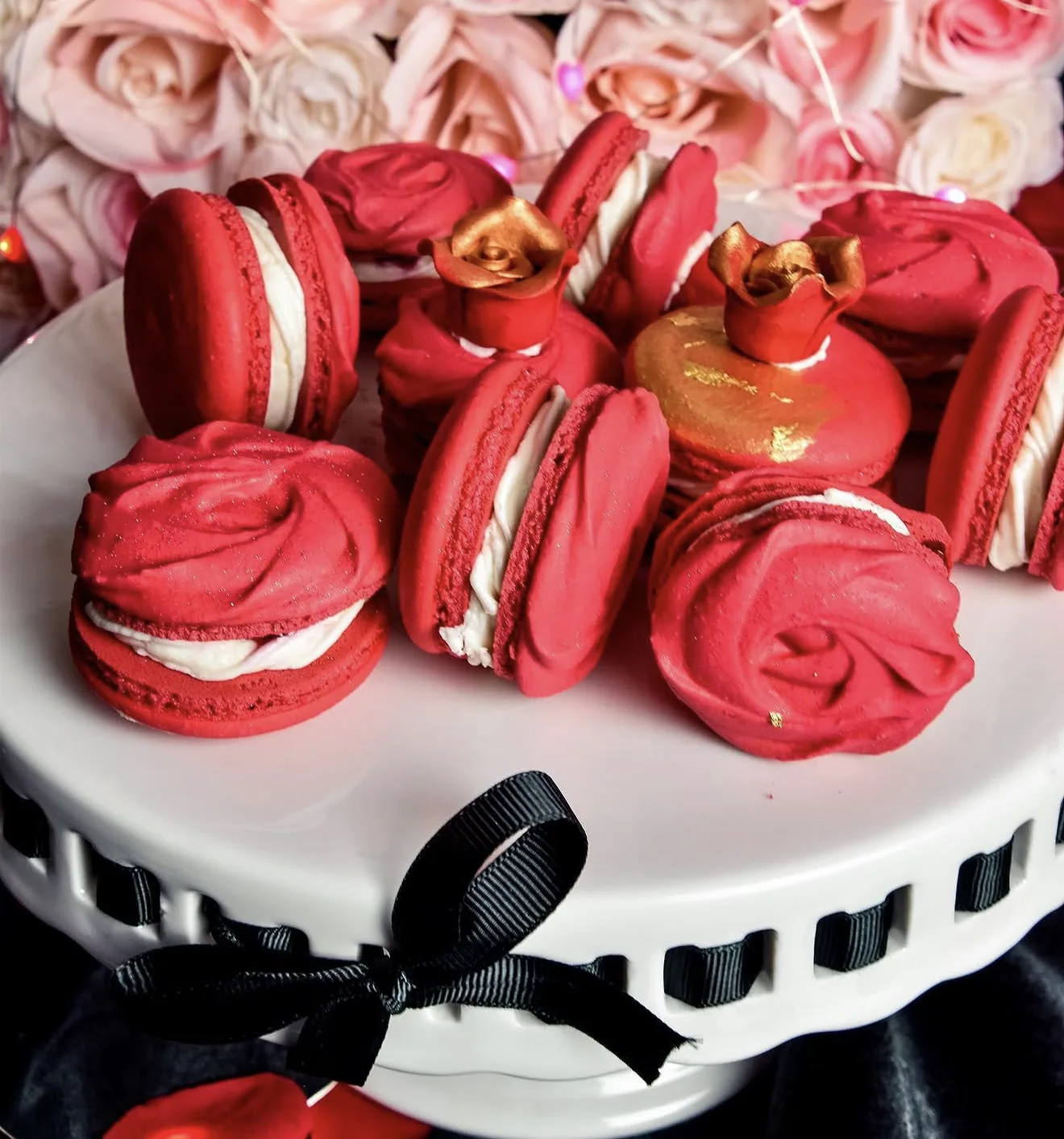 Pink macaron with piped love script resting on white plate beside cream rose on silver cloth