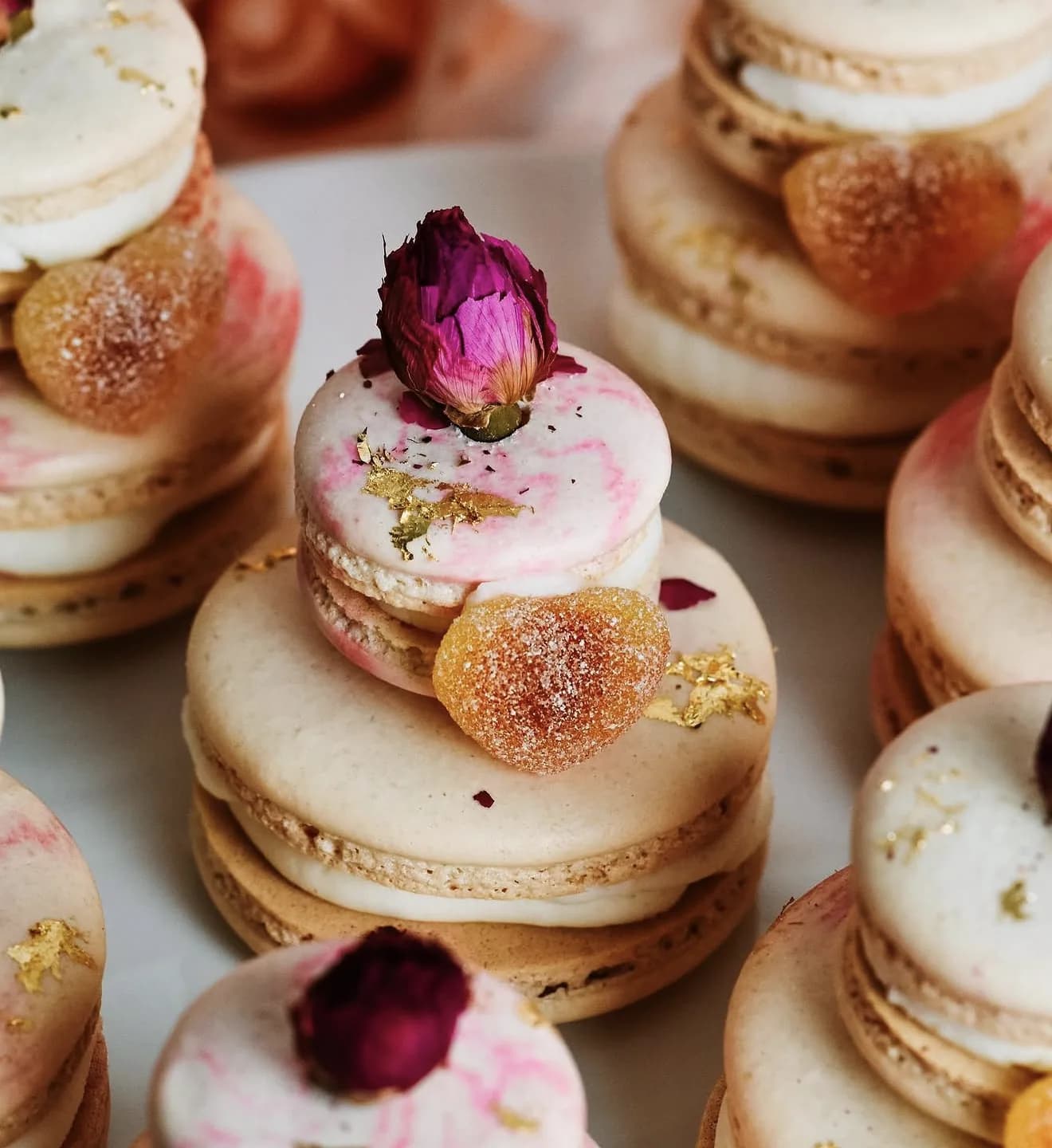 Stacked cream macarons topped with gummy orange hearts pink marble and dried rosebuds