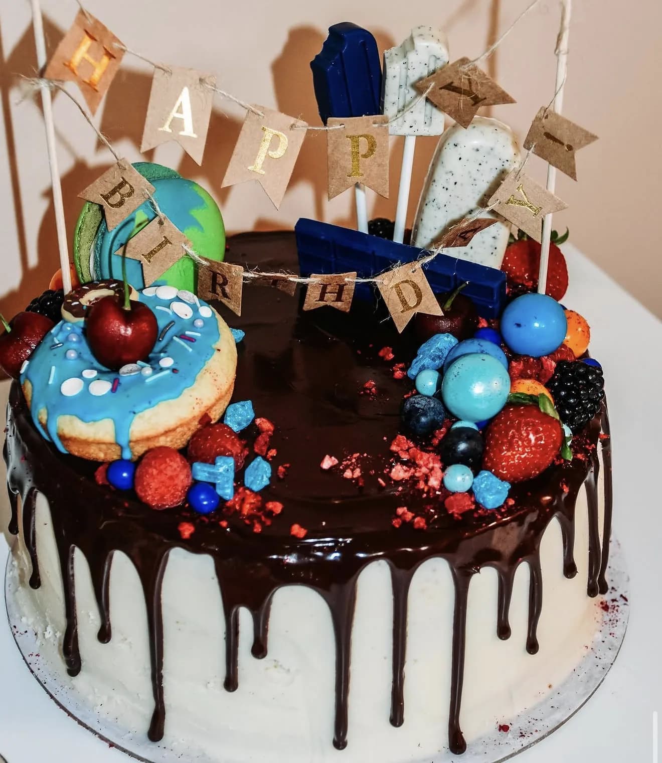 Chocolate drip cake with earth donut planets and space-themed candies atop ganache pool