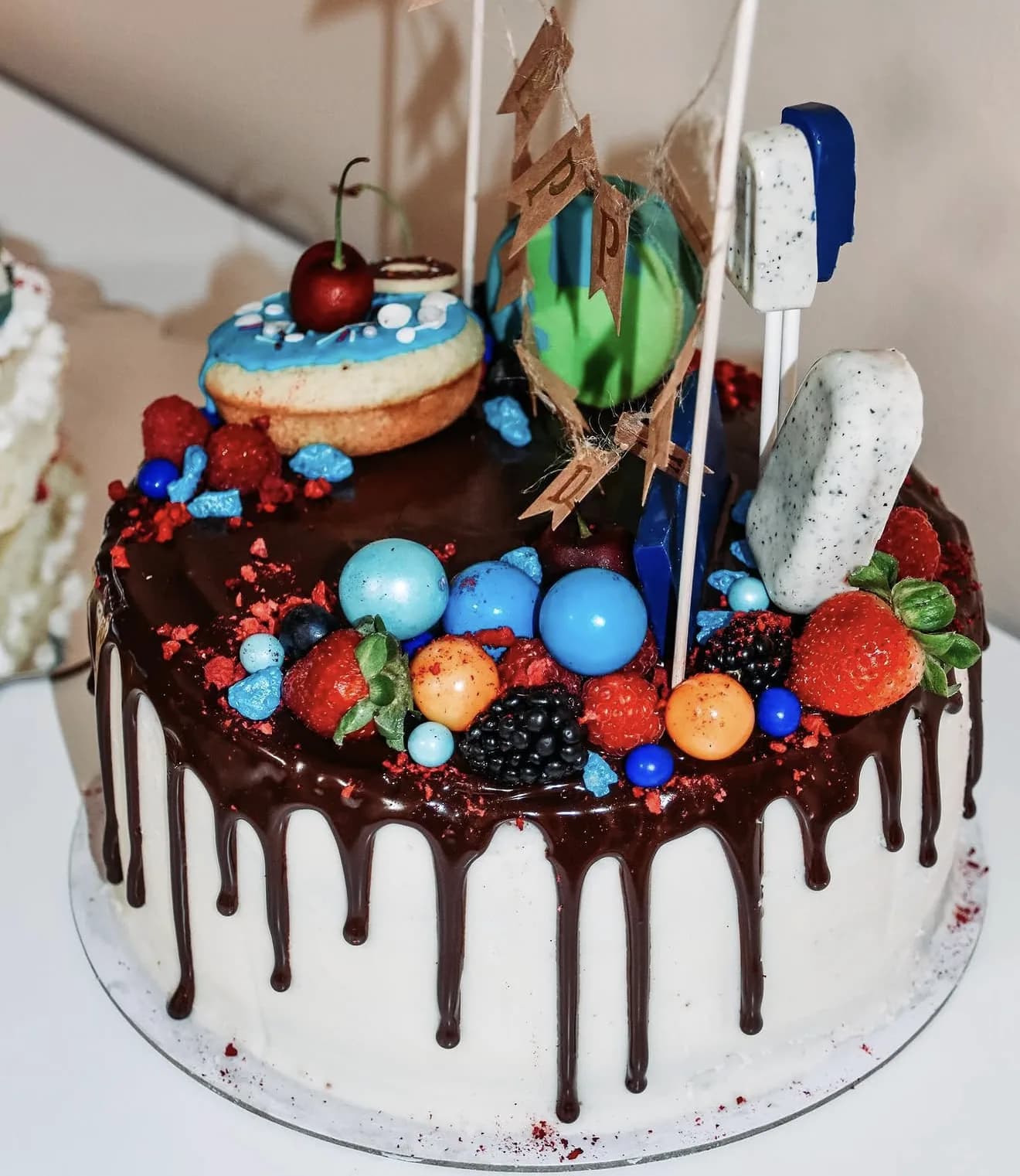 Space themed chocolate drip cake with banner astronaut marshmallow and galaxy sphere candies