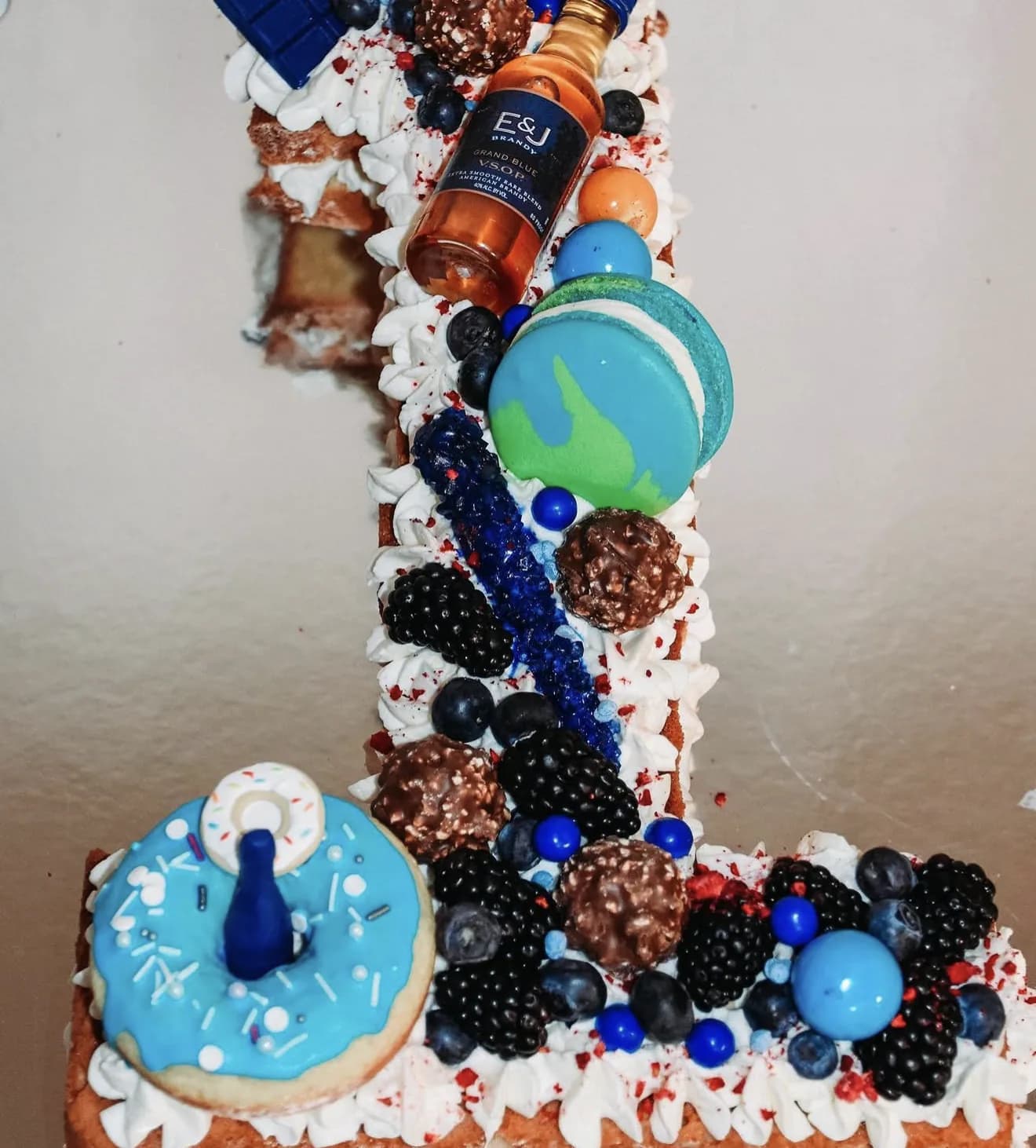 White cake with gold leaf flakes drip coconut bowl of fruit and Happy Birthday geometric topper