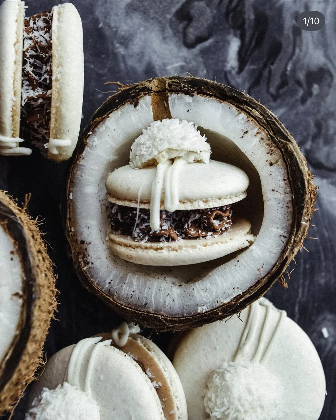 Overhead white raffaello macarons inside split coconut halves with coconut pulp on marble