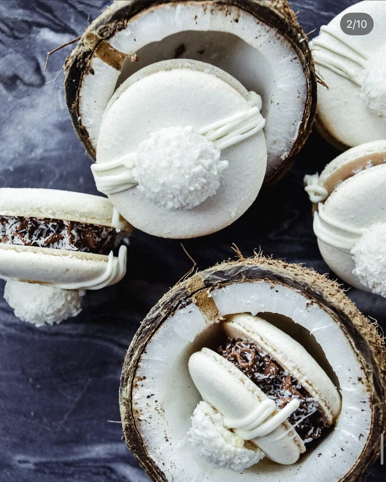 White raffaello macaron with coconut coated filling on marble surface beside coconut half